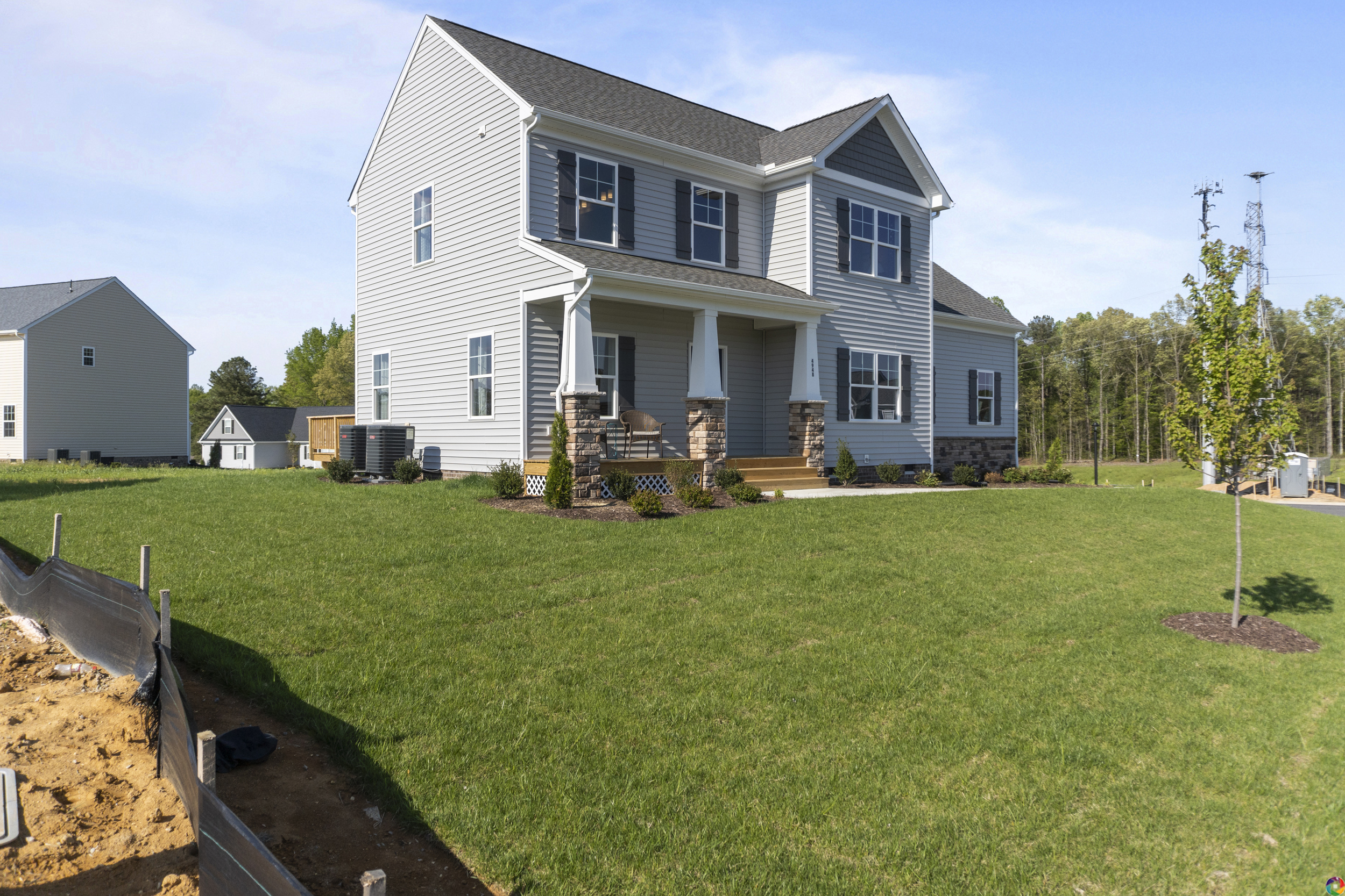 A two-story house with white siding and a gray roof, featuring a front porch with columns, placed on a large grass lawn with minimal landscaping and an unfinished area near the left.