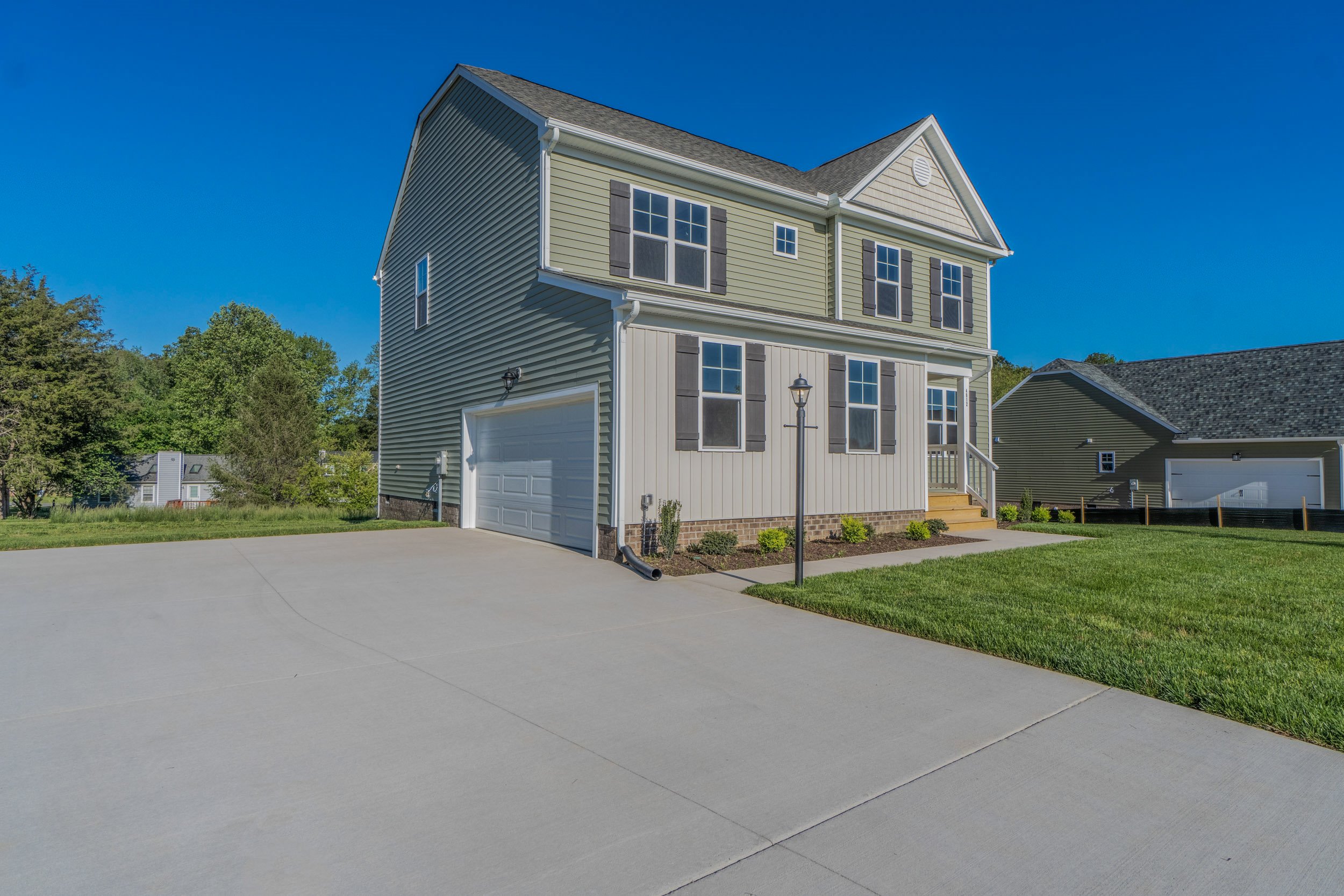 Two-story house with gray siding, white trim, double garage, and well-maintained lawn, set against a bright blue sky.