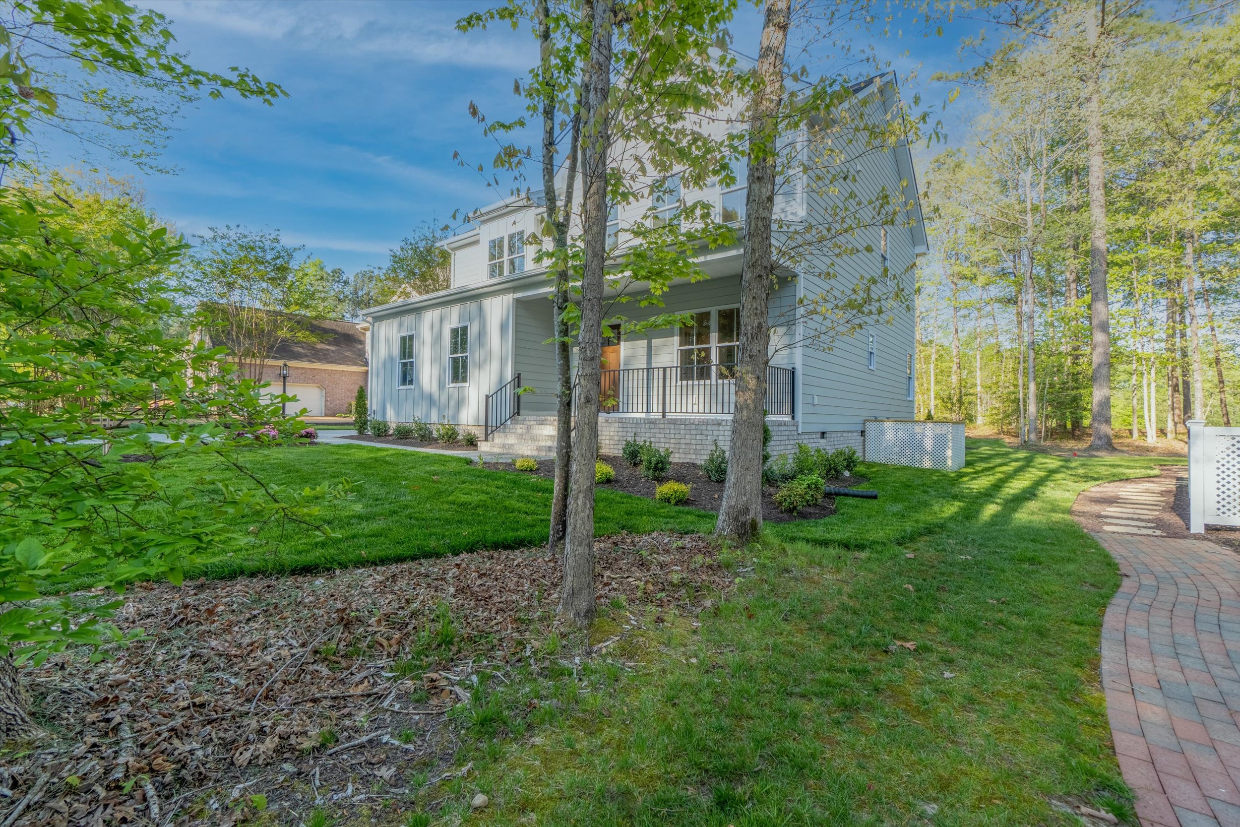 A two-story house with a porch, surrounded by lush green grass and trees, with a brick pathway leading to the entrance on a sunny day.