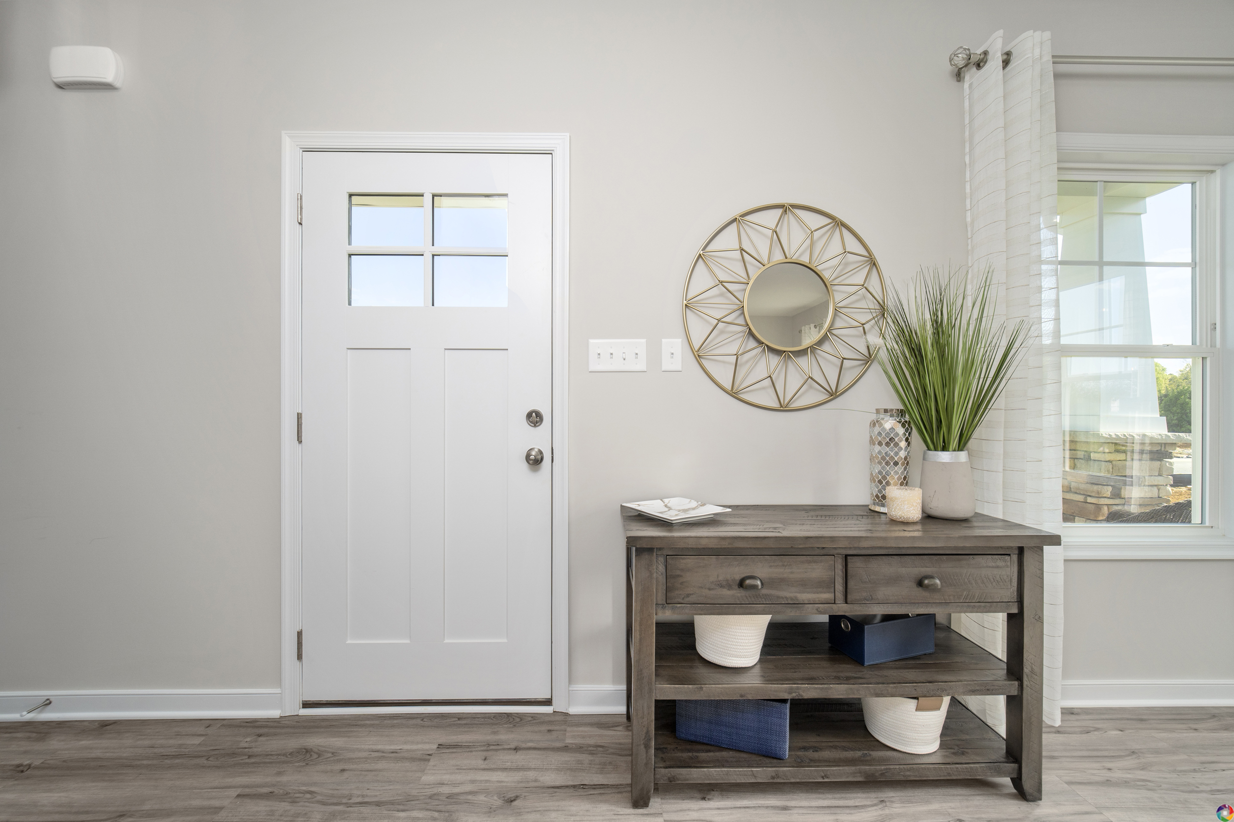 Modern entryway with a white front door, wooden console table with baskets, and a round mirror on the wall.