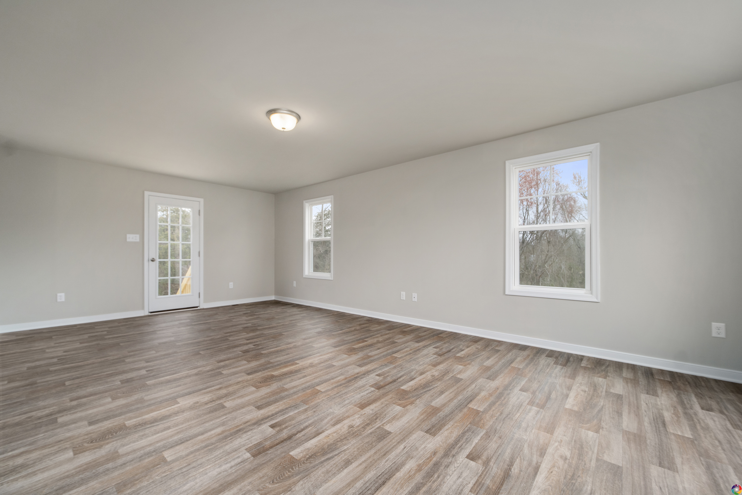 An empty room with smooth wood-look flooring, light gray walls, two windows, and a door leading outside, illuminated by a semi-flush ceiling light.
