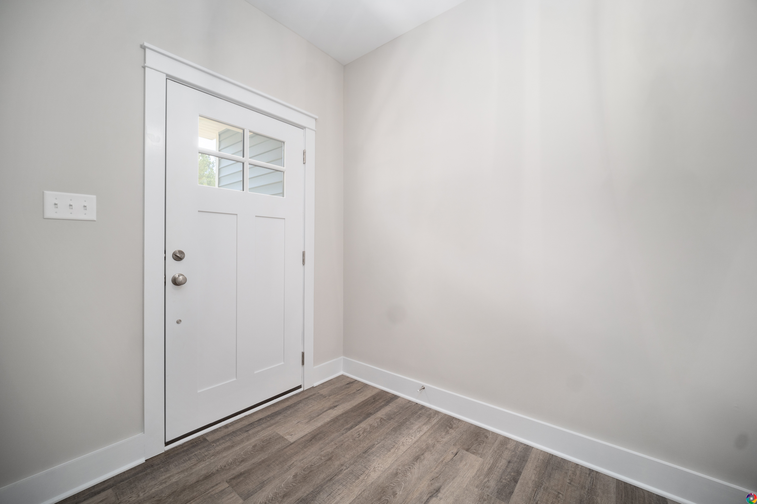 A white door with a windowpane at the top, located in a small entryway with light gray walls and wood-textured flooring.