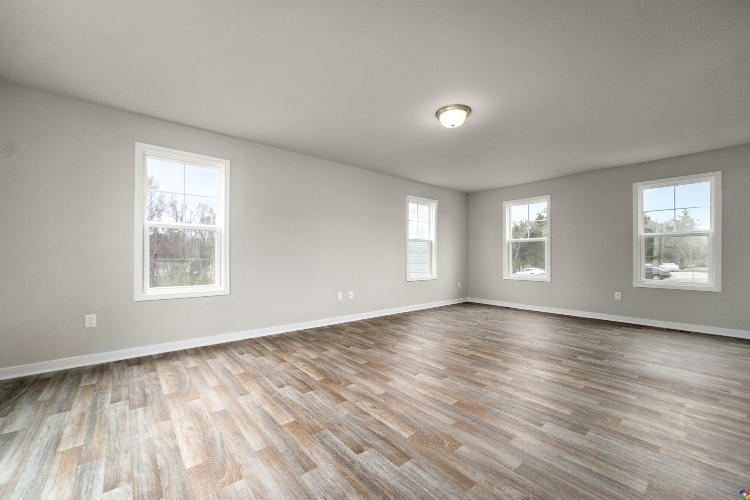 Empty living room with hardwood flooring, three windows, and a ceiling light in a new house.