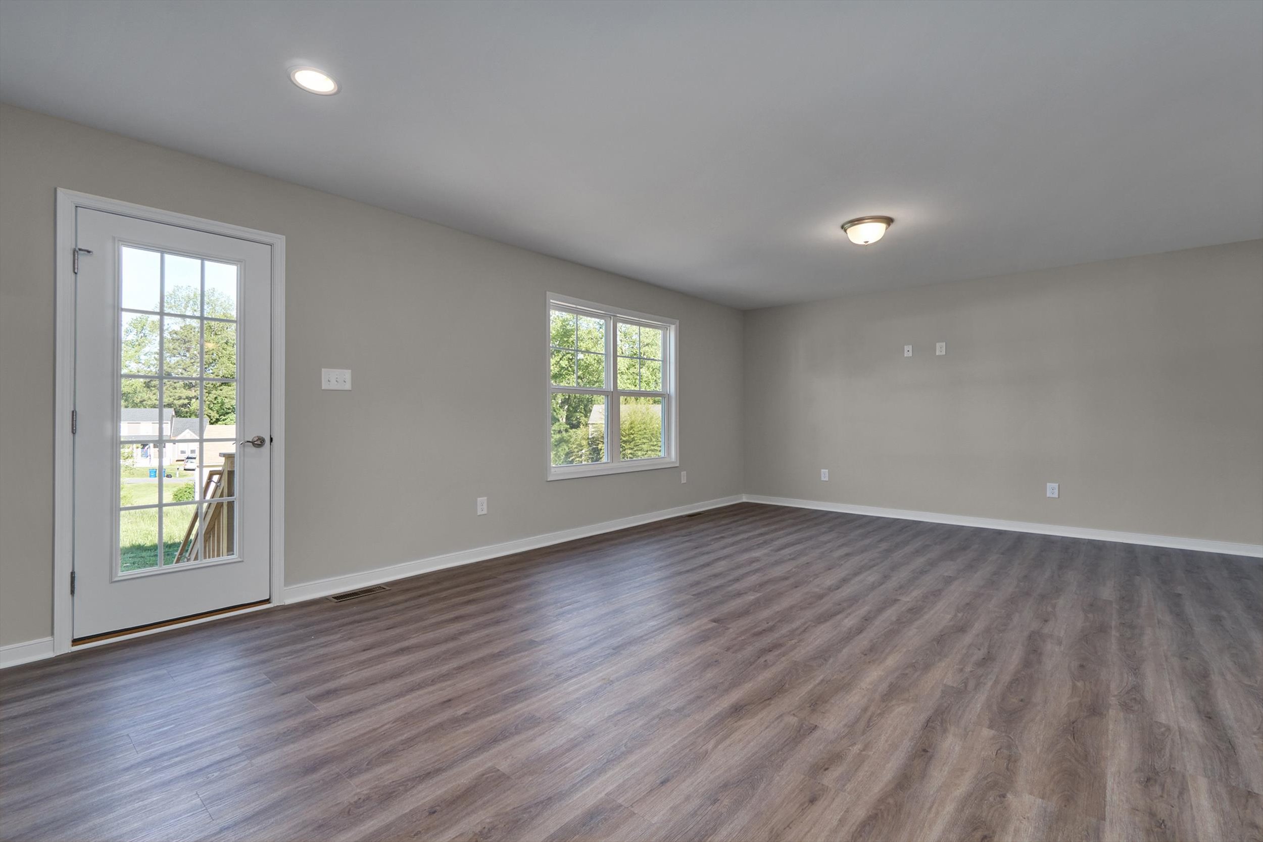 An empty room with gray walls, wood flooring, a window, a door, and a ceiling light fixture.