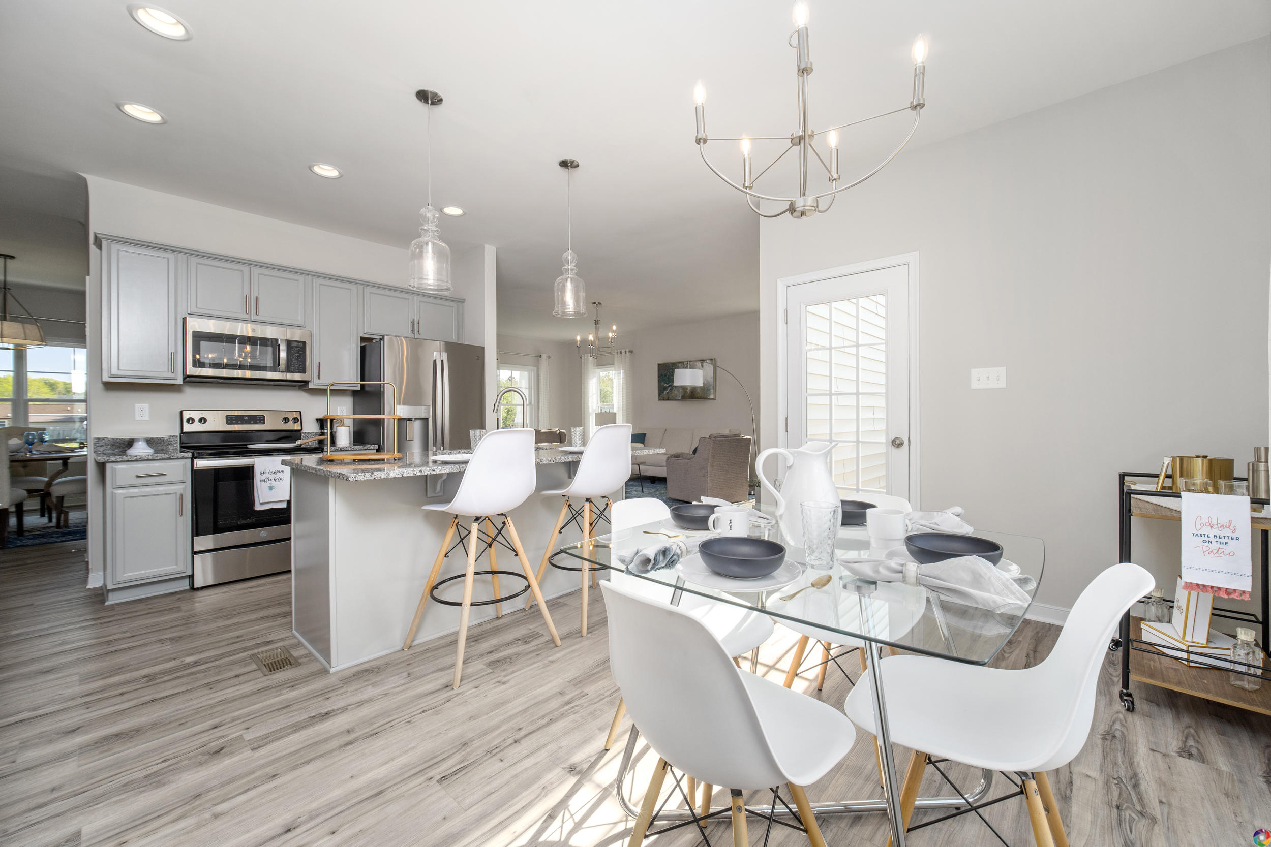 Modern kitchen and dining area with white cabinetry, stainless steel appliances, a dining table set for four, and pendant lighting.