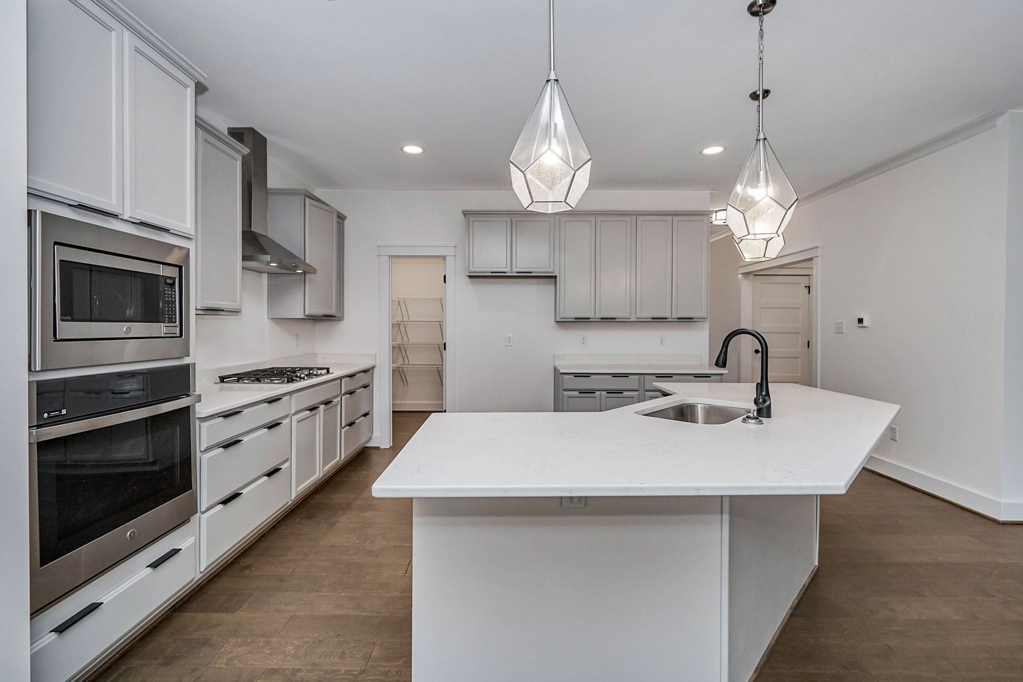 Modern kitchen with white cabinets, stainless steel appliances, and a large central island with a sink. The kitchen features pendant lighting and hardwood flooring.