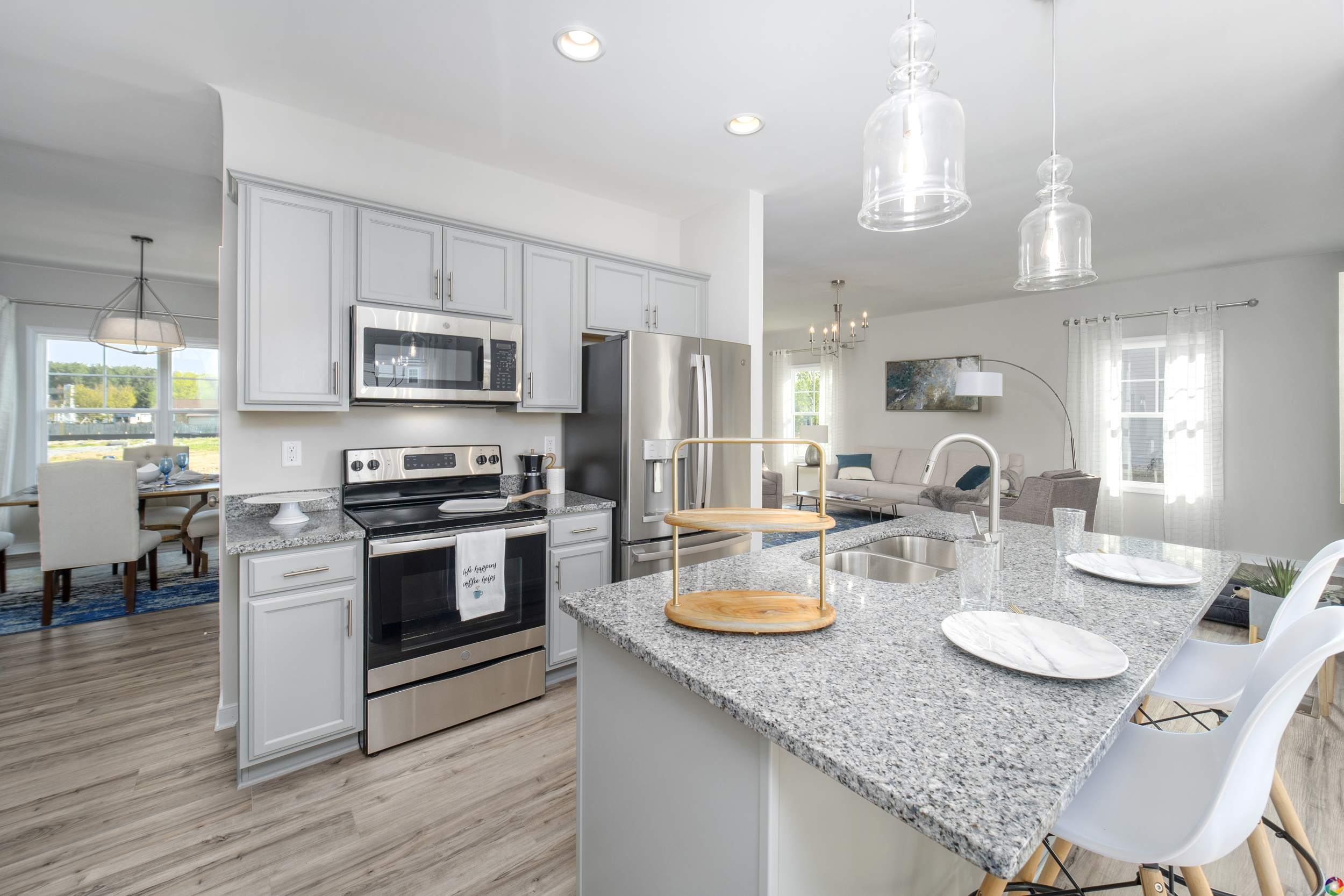 Modern kitchen with stainless steel appliances, granite countertops, and pendant lights, opening to a dining area.