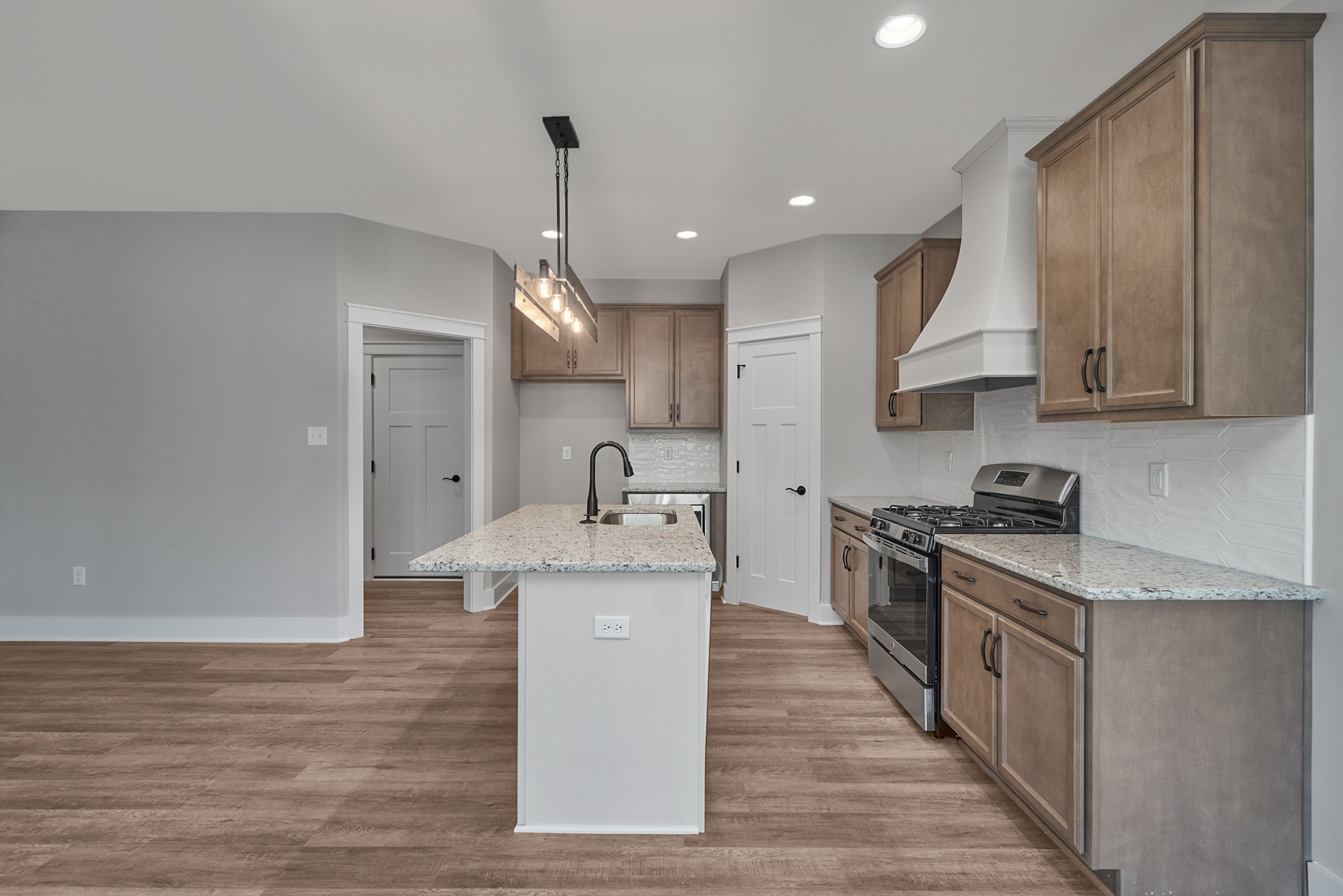 Modern kitchen with hardwood floors, wooden cabinets, granite countertops, stainless steel appliances, central island with sink, and pendant lighting.