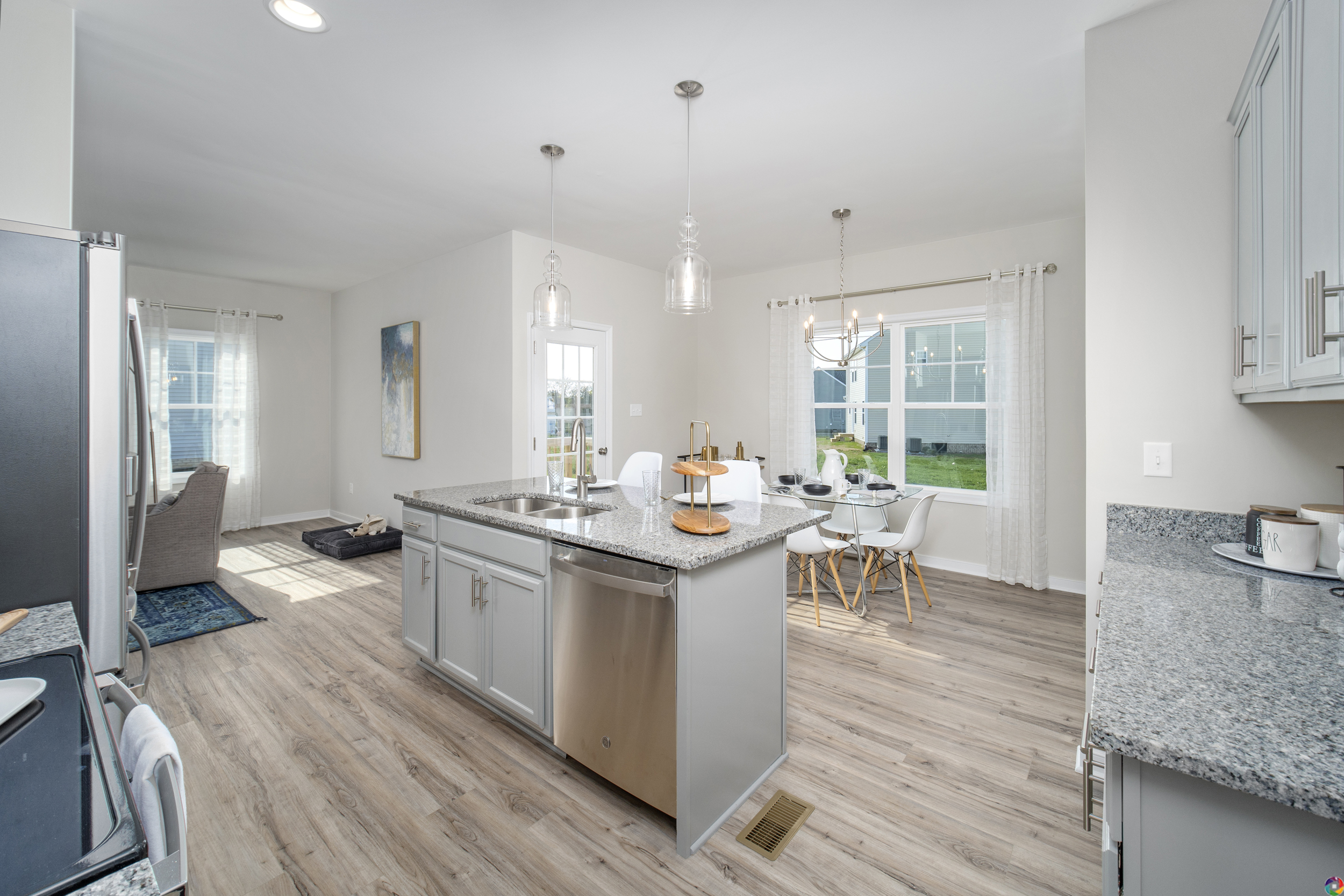 Modern kitchen with stainless steel appliances, island, pendant lights, and an open plan layout extending to a dining area with a table, chairs, and visible living room.