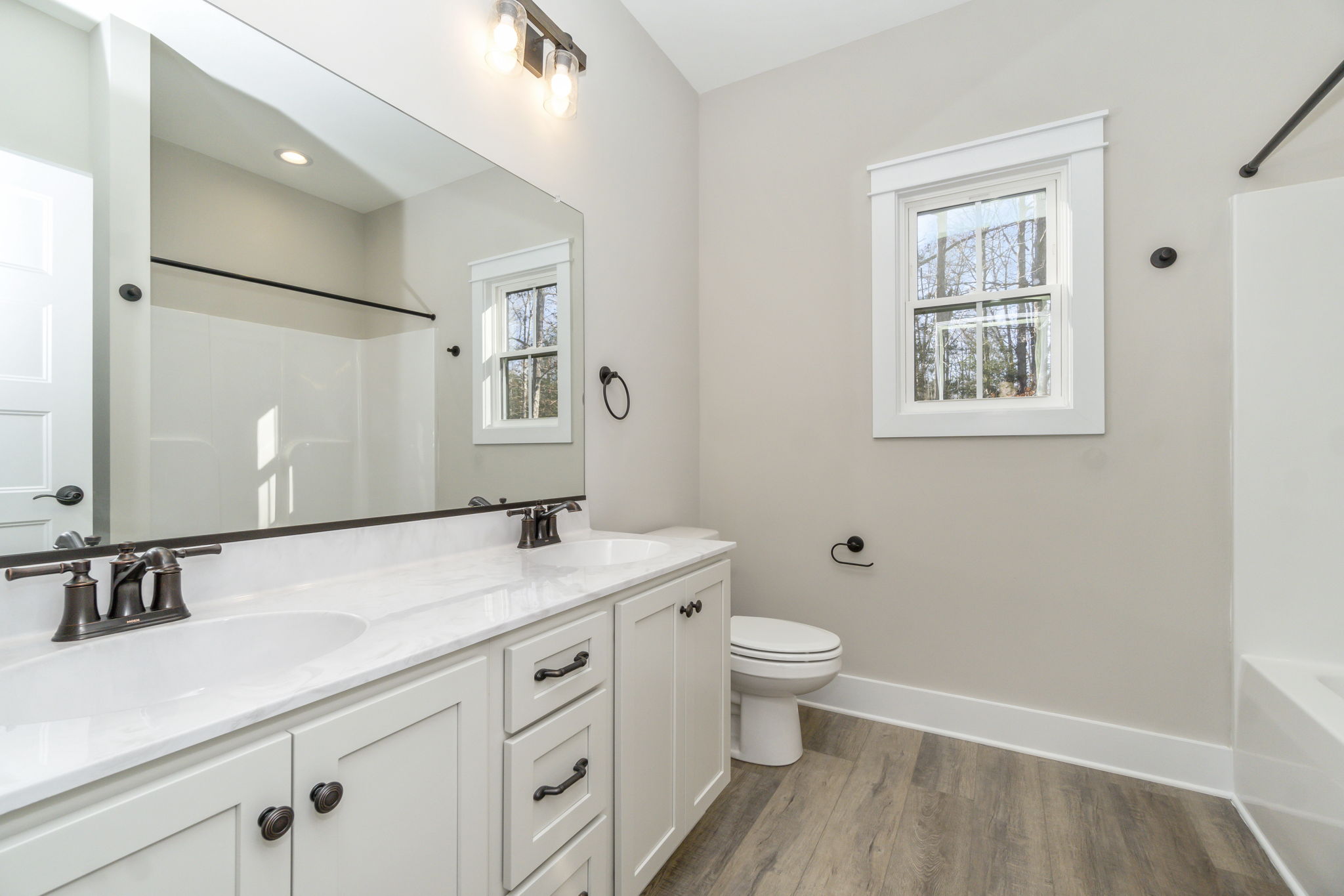 Modern bathroom interior featuring a white vanity with double sinks, large mirror, glass shower stall, and two windows.