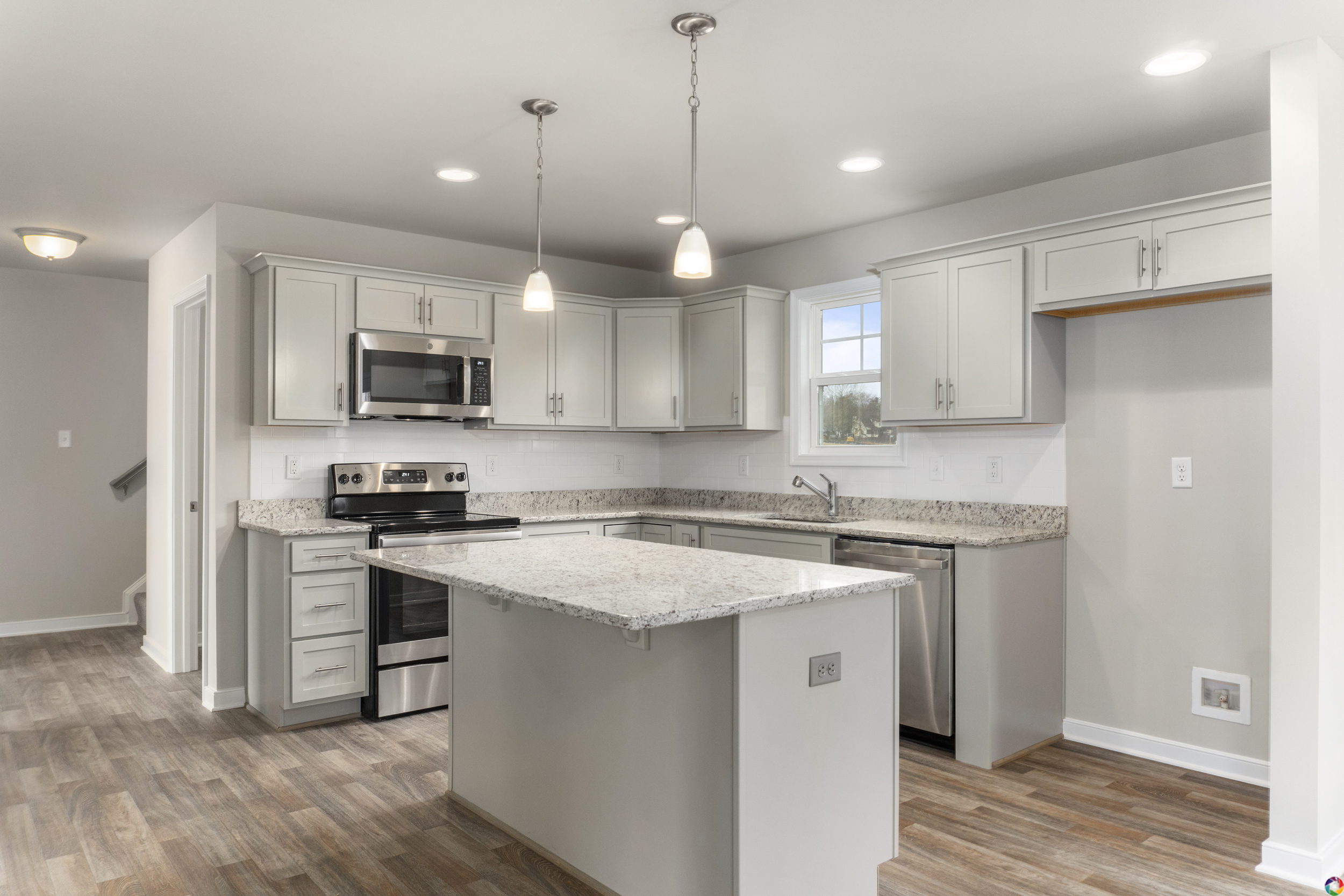 A modern kitchen with stainless steel appliances, white cabinets, a large island with a granite countertop, hardwood floors, and pendant lighting.
