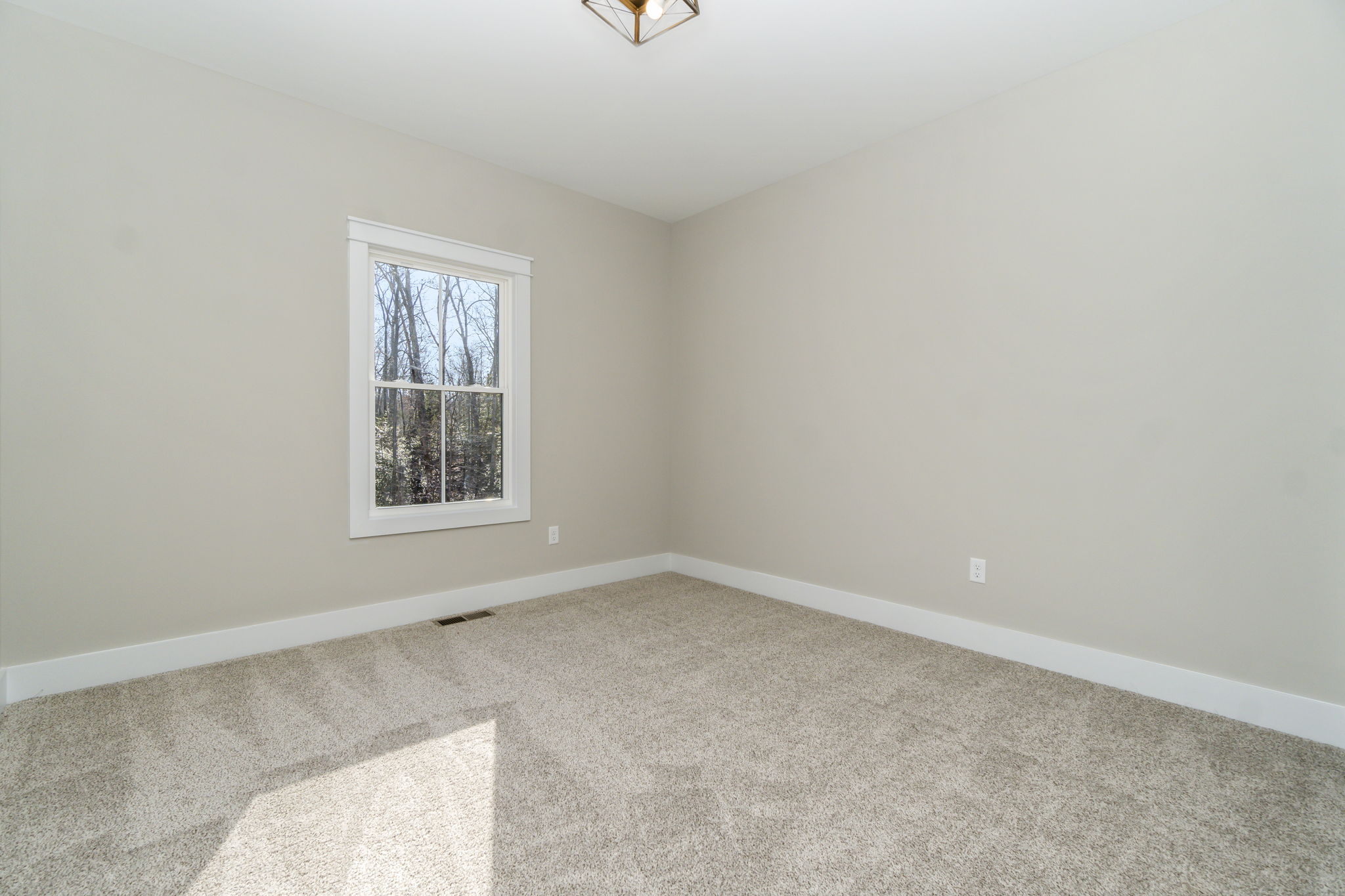 Empty room with gray walls, a single window letting in natural light, and beige carpeted flooring.