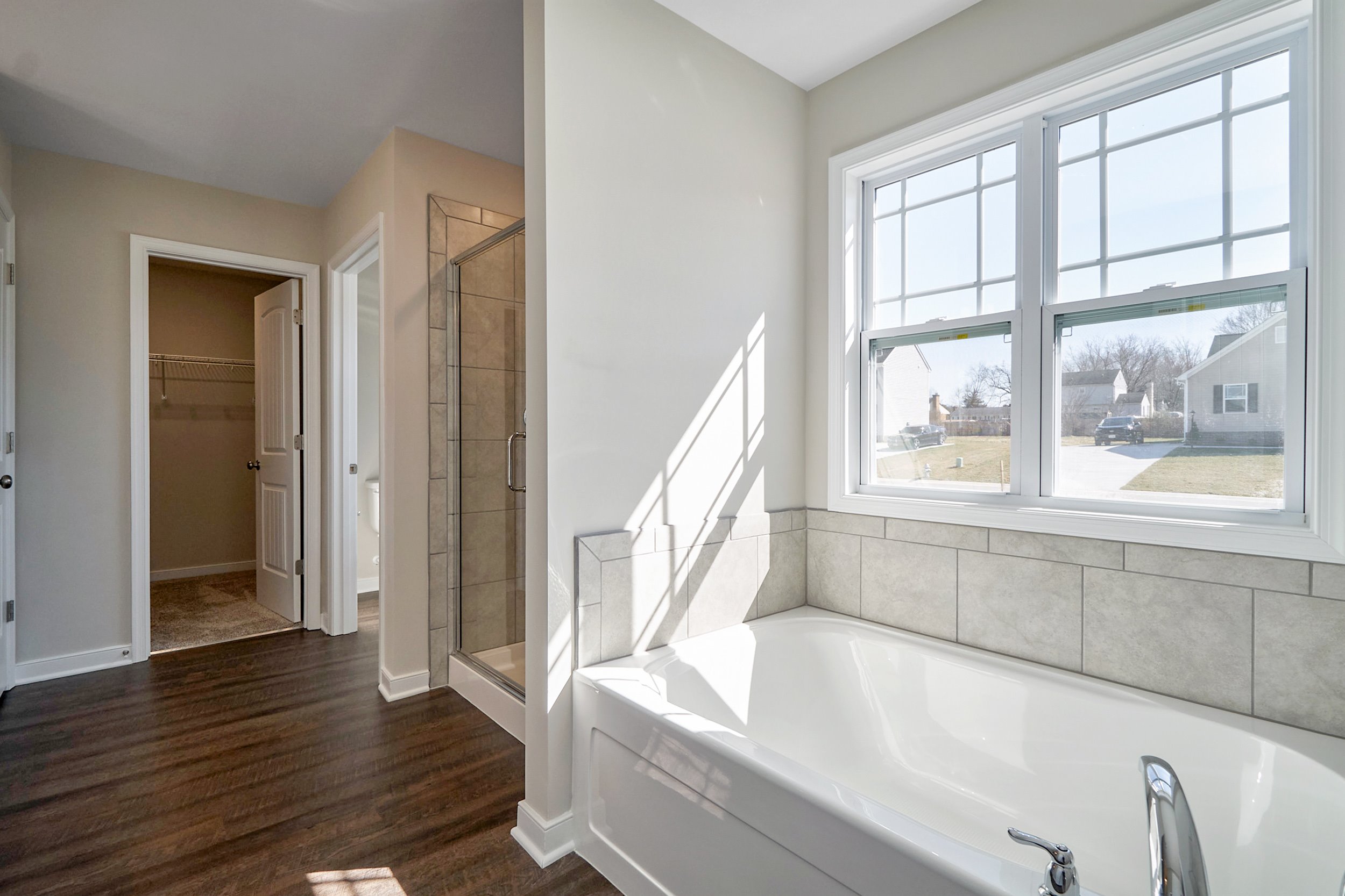 Modern bathroom interior with a large bathtub by a window, hardwood floors, and a glass shower door.