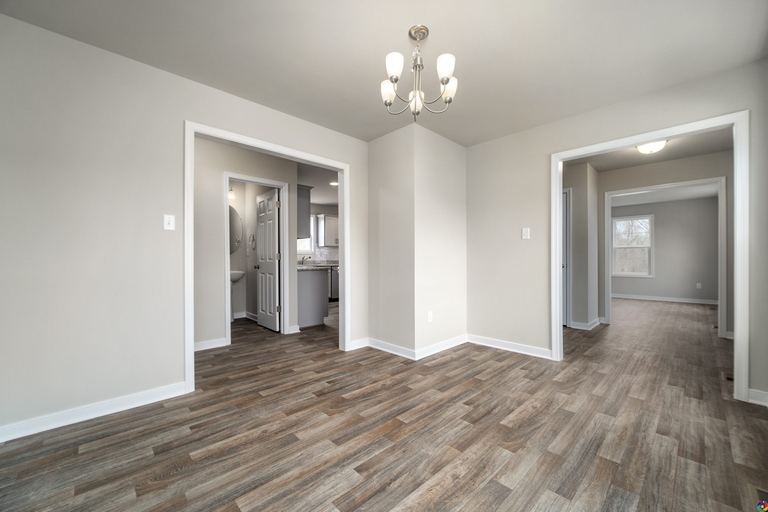 Empty room with light gray walls, wood-look flooring, a decorative light fixture on the ceiling, and doorways leading to adjacent rooms.