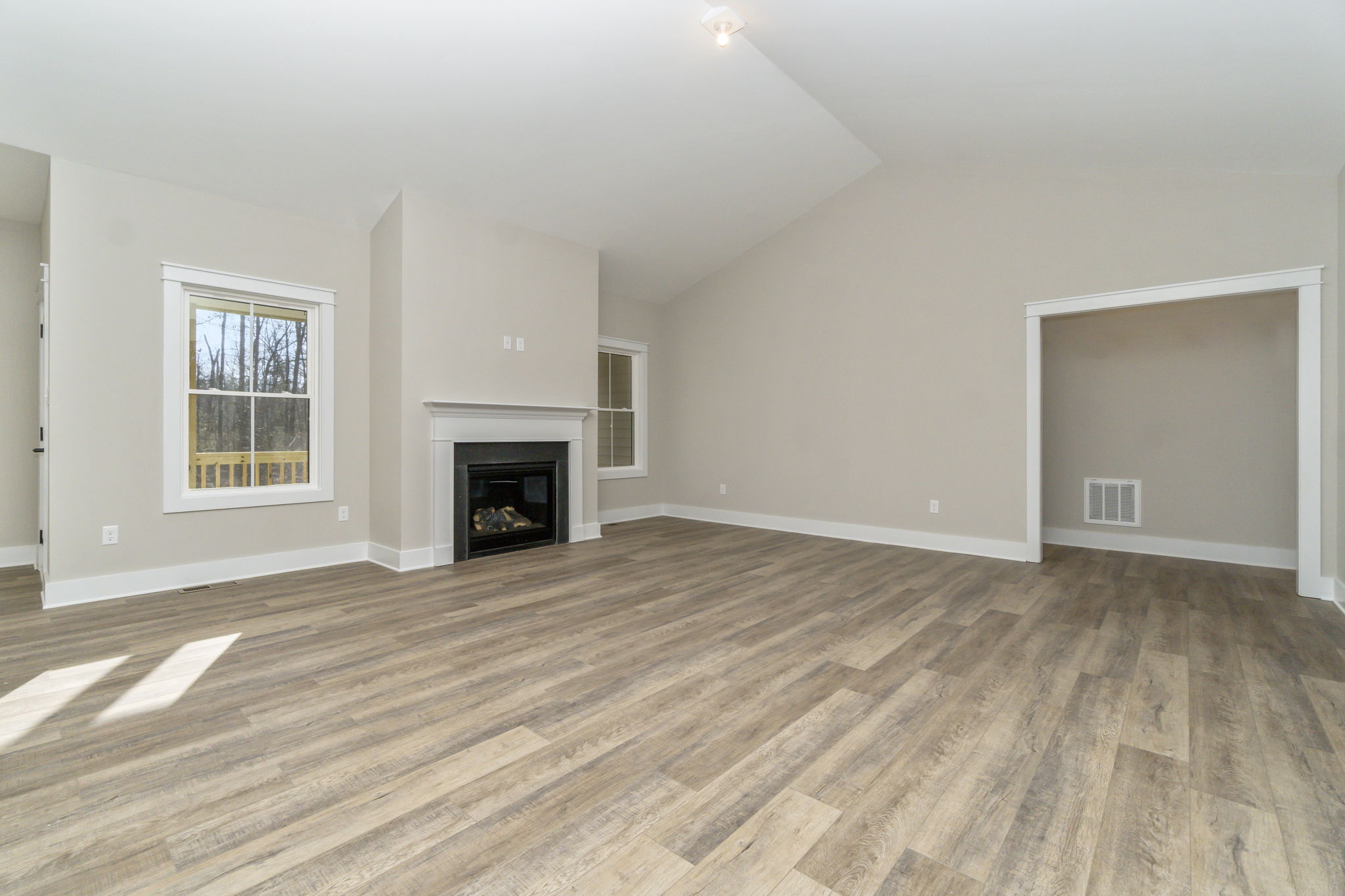 Empty living room with beige walls, vinyl flooring, a fireplace, and sunlight casting shadows on the floor.