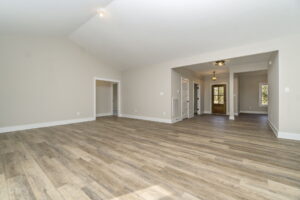 Empty living room with beige walls, wooden floors, and multiple doorways, featuring recessed lighting.