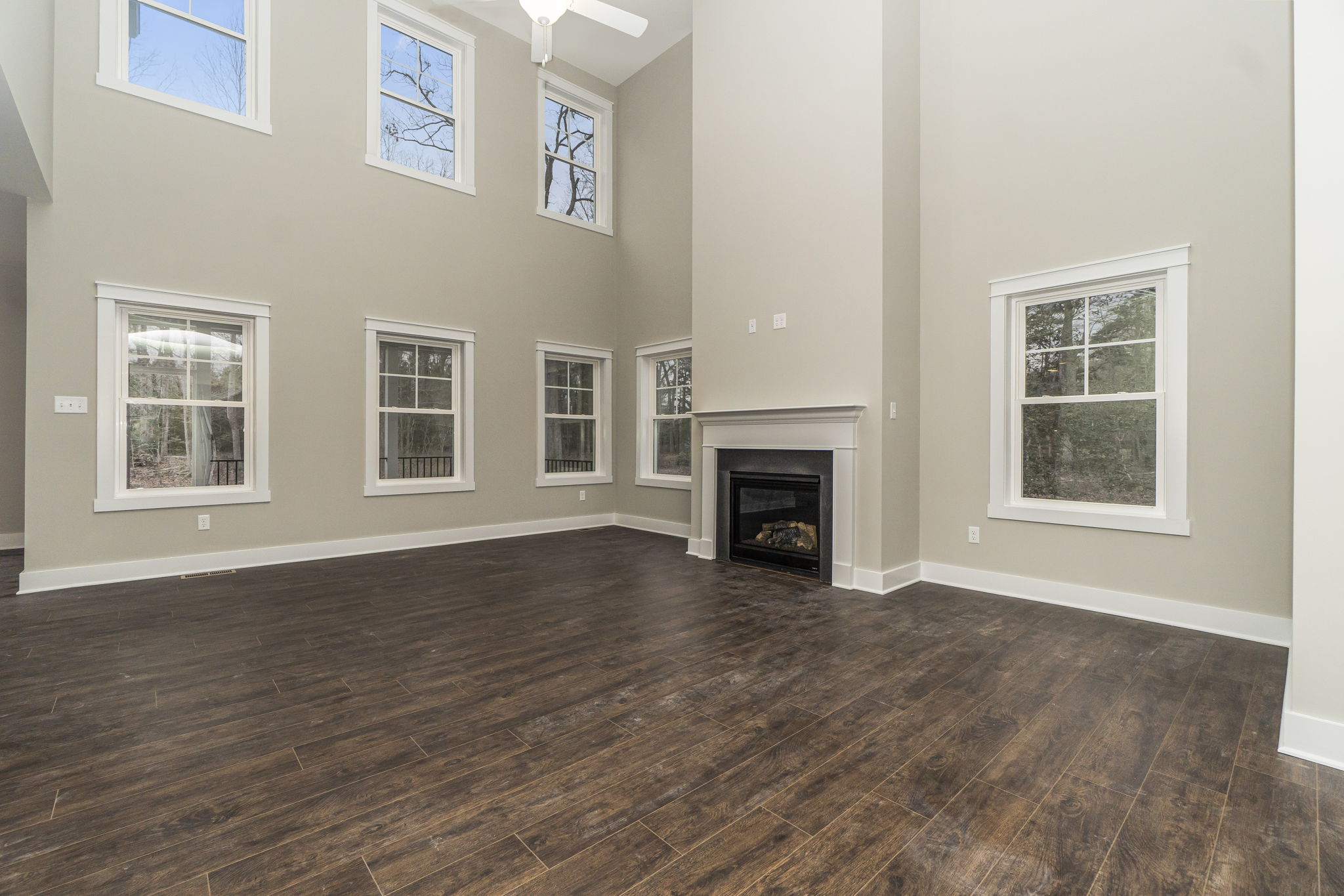 A spacious, empty living room with high ceilings, a fireplace, multiple windows, and dark hardwood flooring.