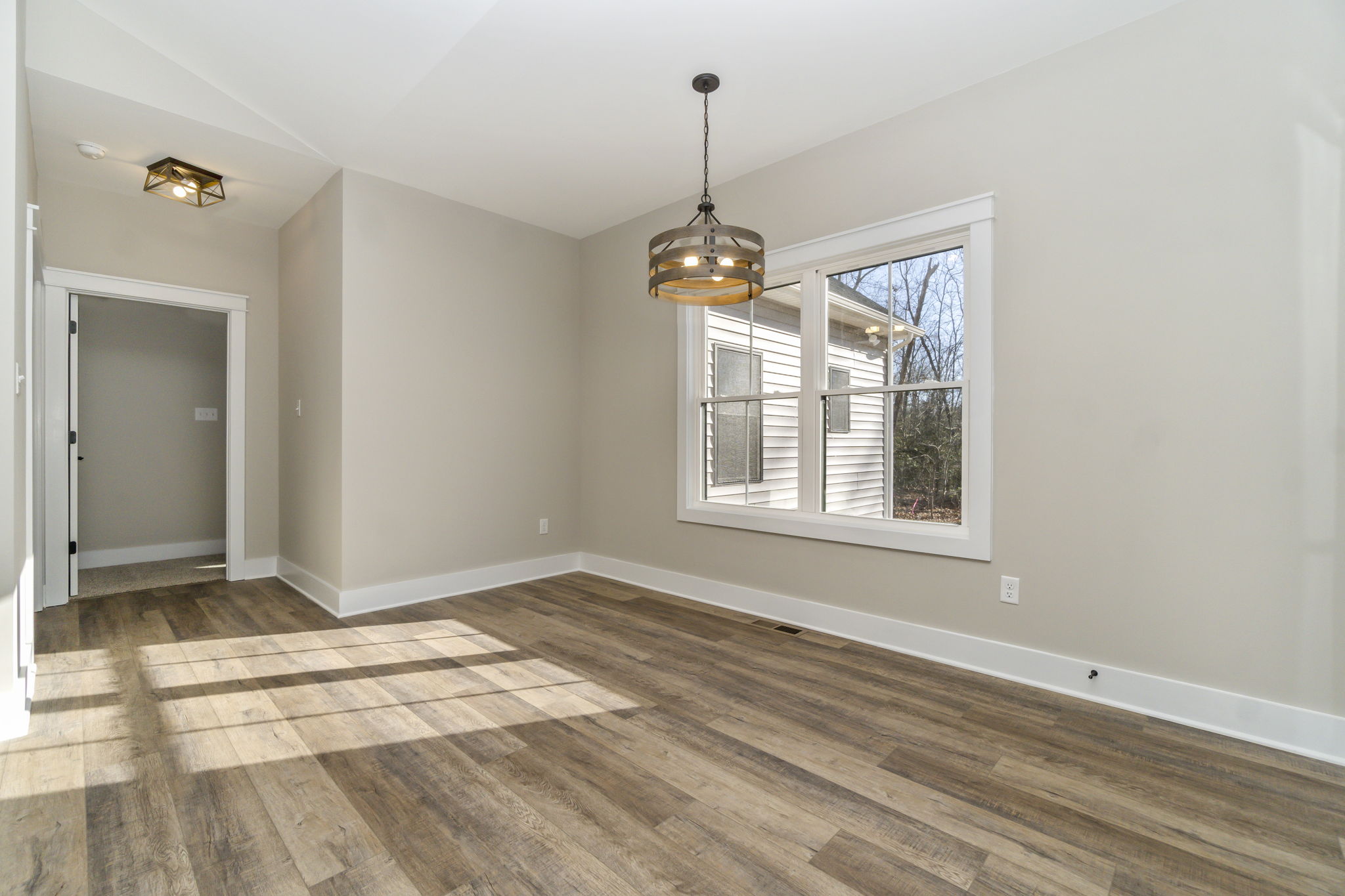 Empty modern living room with hardwood floors, large window, and a hanging light fixture.