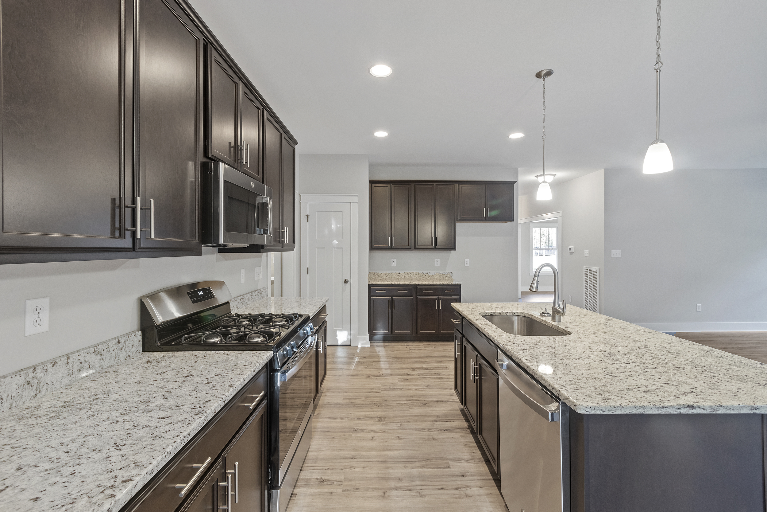 Modern kitchen with dark wooden cabinets, stainless steel appliances, including a gas stove and dishwasher, granite countertops, a large island with a sink, and hardwood flooring.