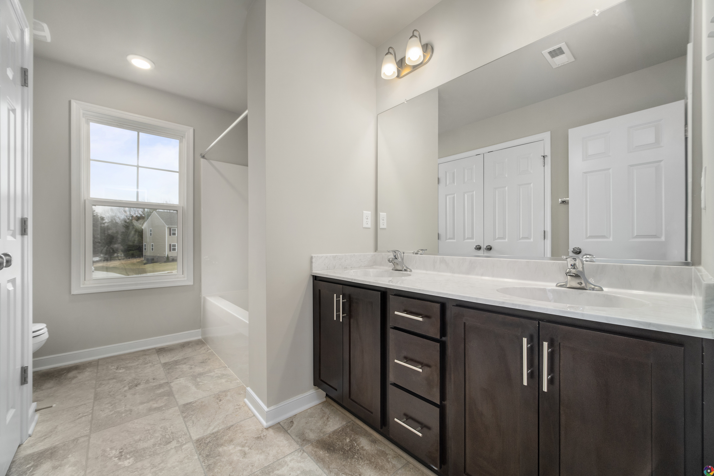Modern bathroom interior with double vanity, large mirror, tiled floor, and a window providing natural light.
