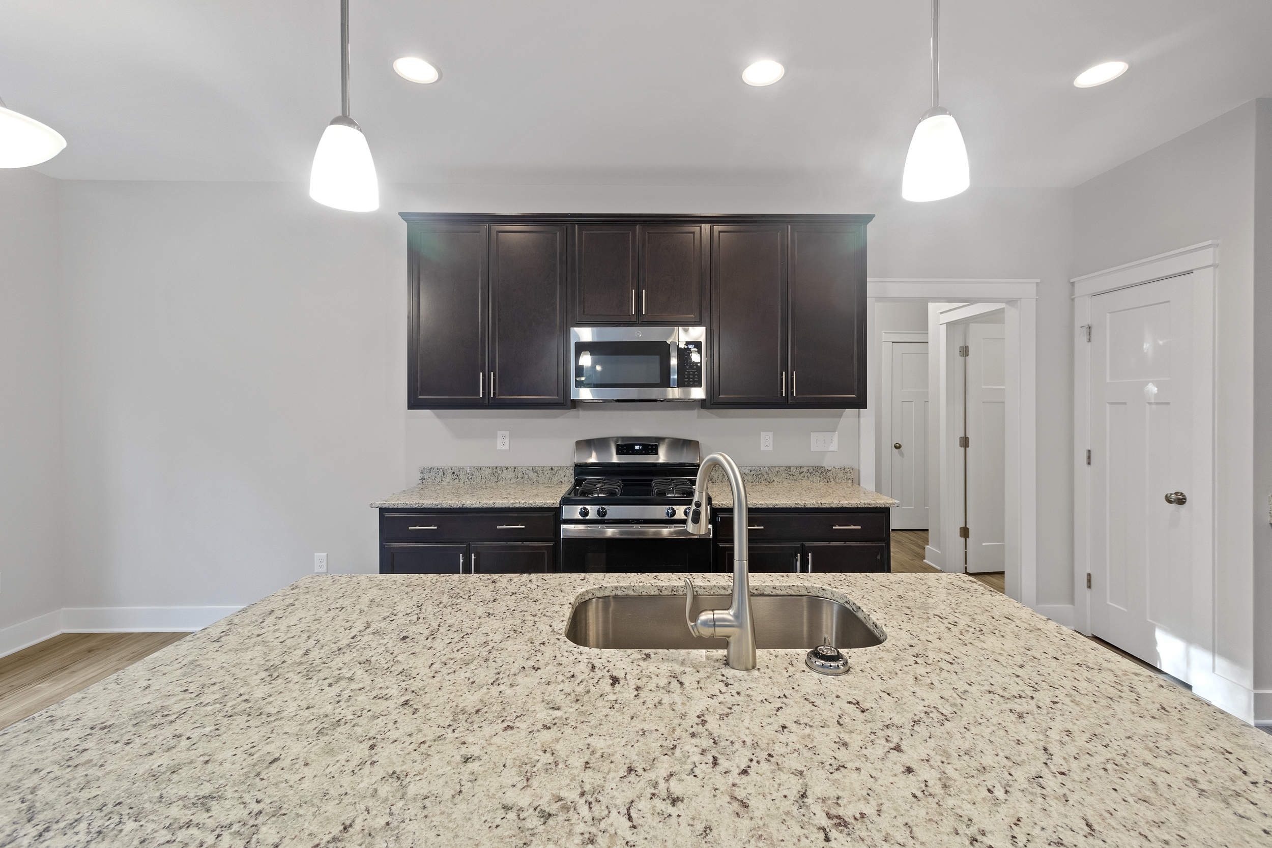 Modern kitchen with dark wood cabinets, stainless steel appliances, and granite countertops featuring a central island with an integrated sink and contemporary pendant lighting.