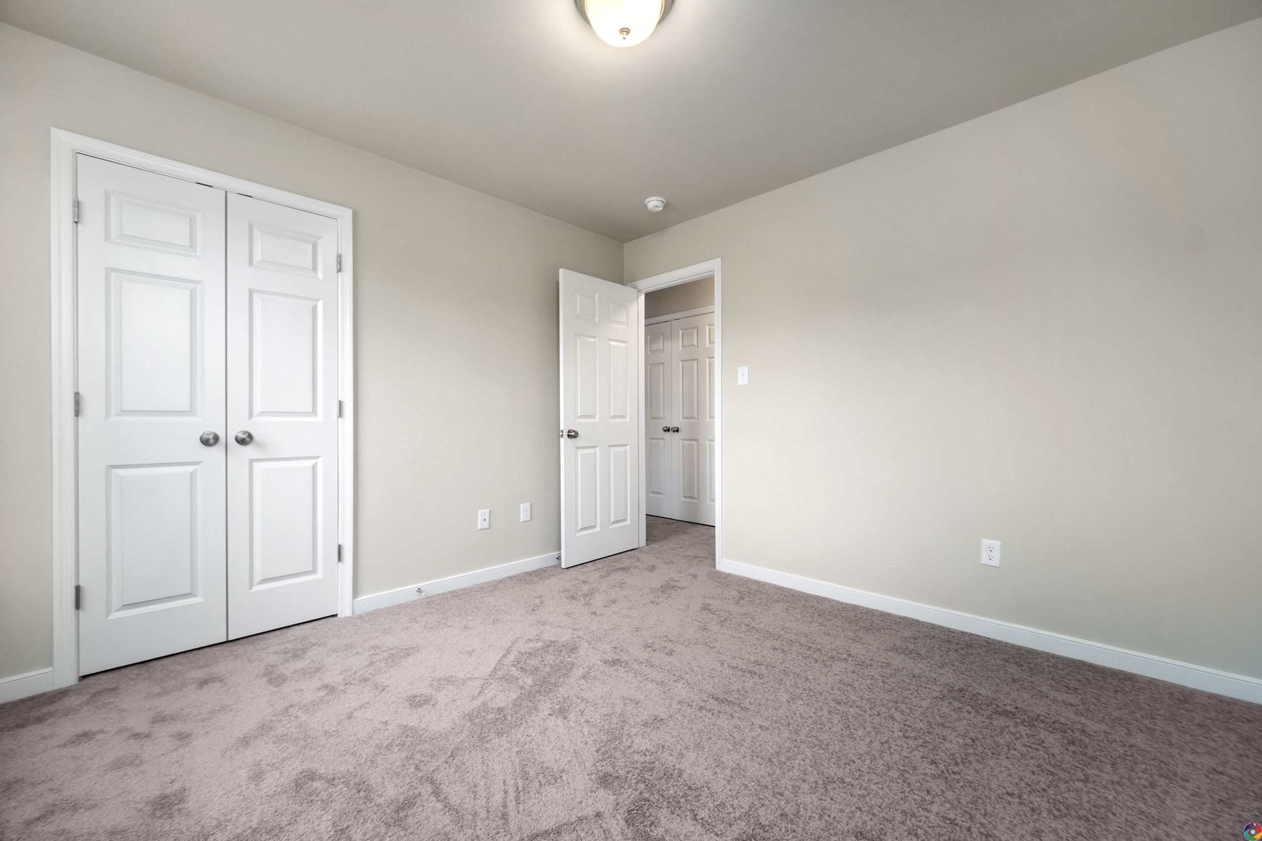 Empty room with light gray walls, plush gray carpet, and three white doors.