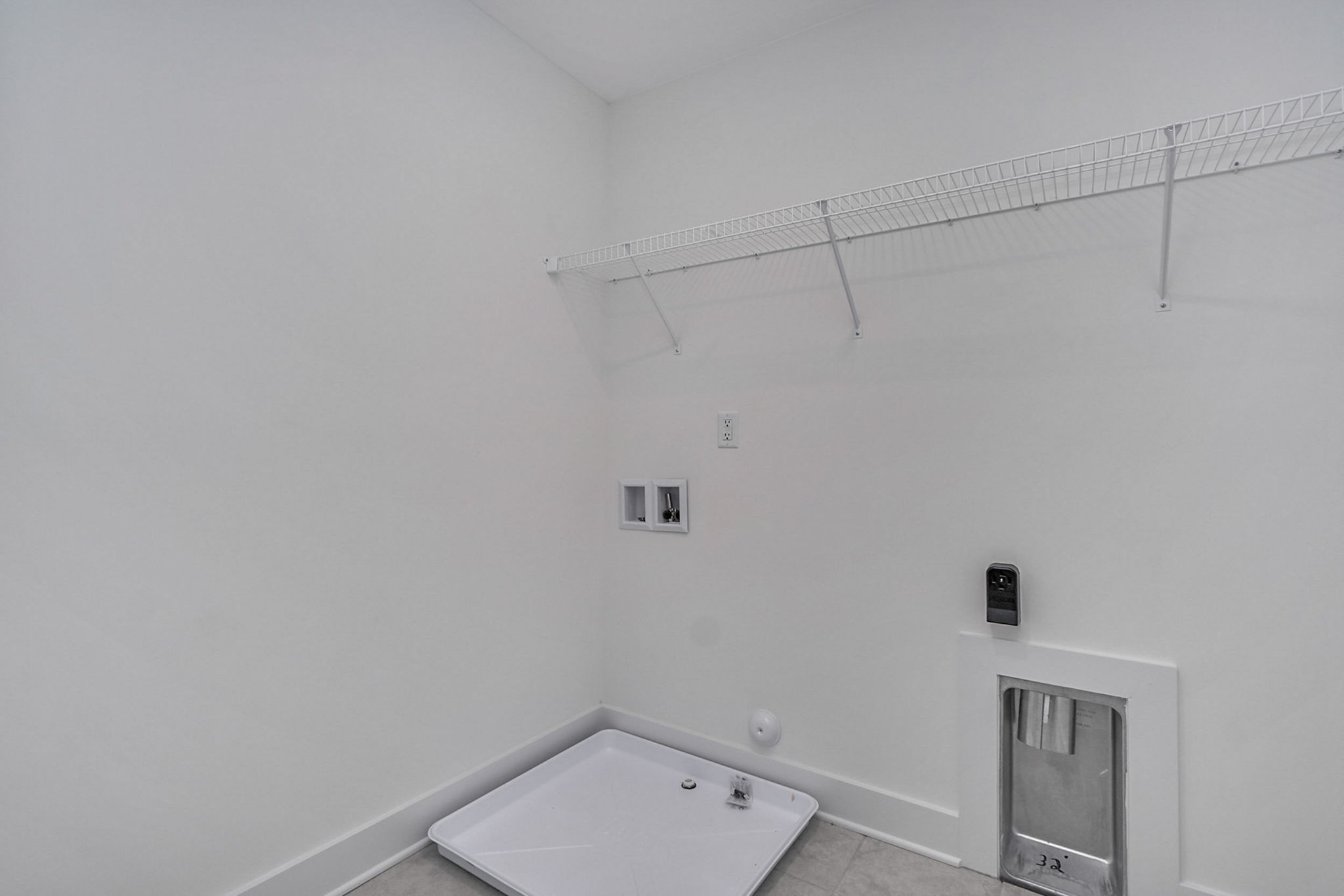 Empty laundry room with a white wire shelf, washer and dryer hookups, a designated area for appliances, and a small pet door on the right side.