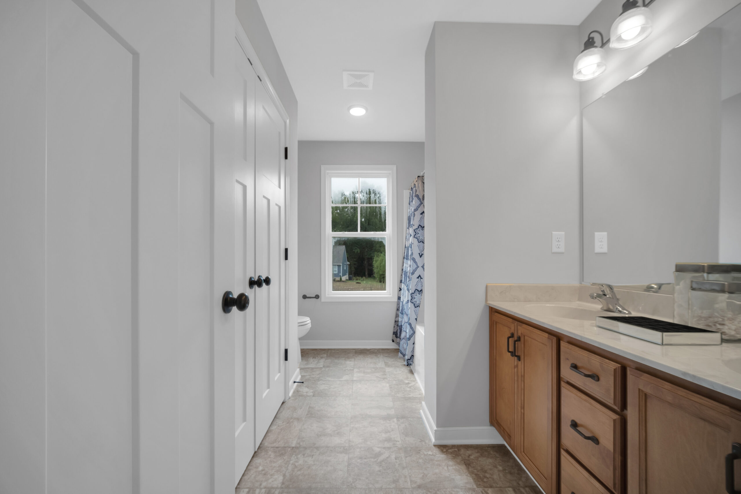 Modern bathroom interior with wooden vanity, tiled floor, white walls, and a view through the window.