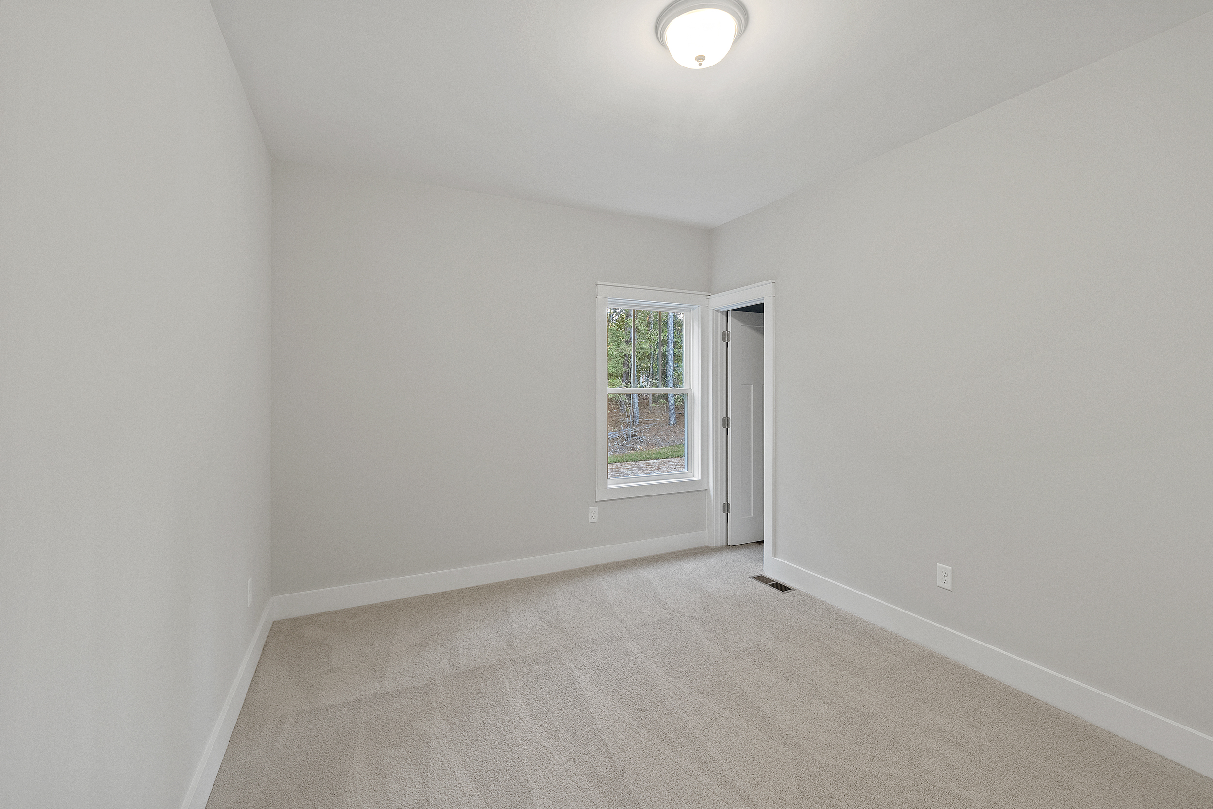 Empty room with beige carpet, gray walls, a window, and a closed door on the right side. Ceiling light fixture is on.