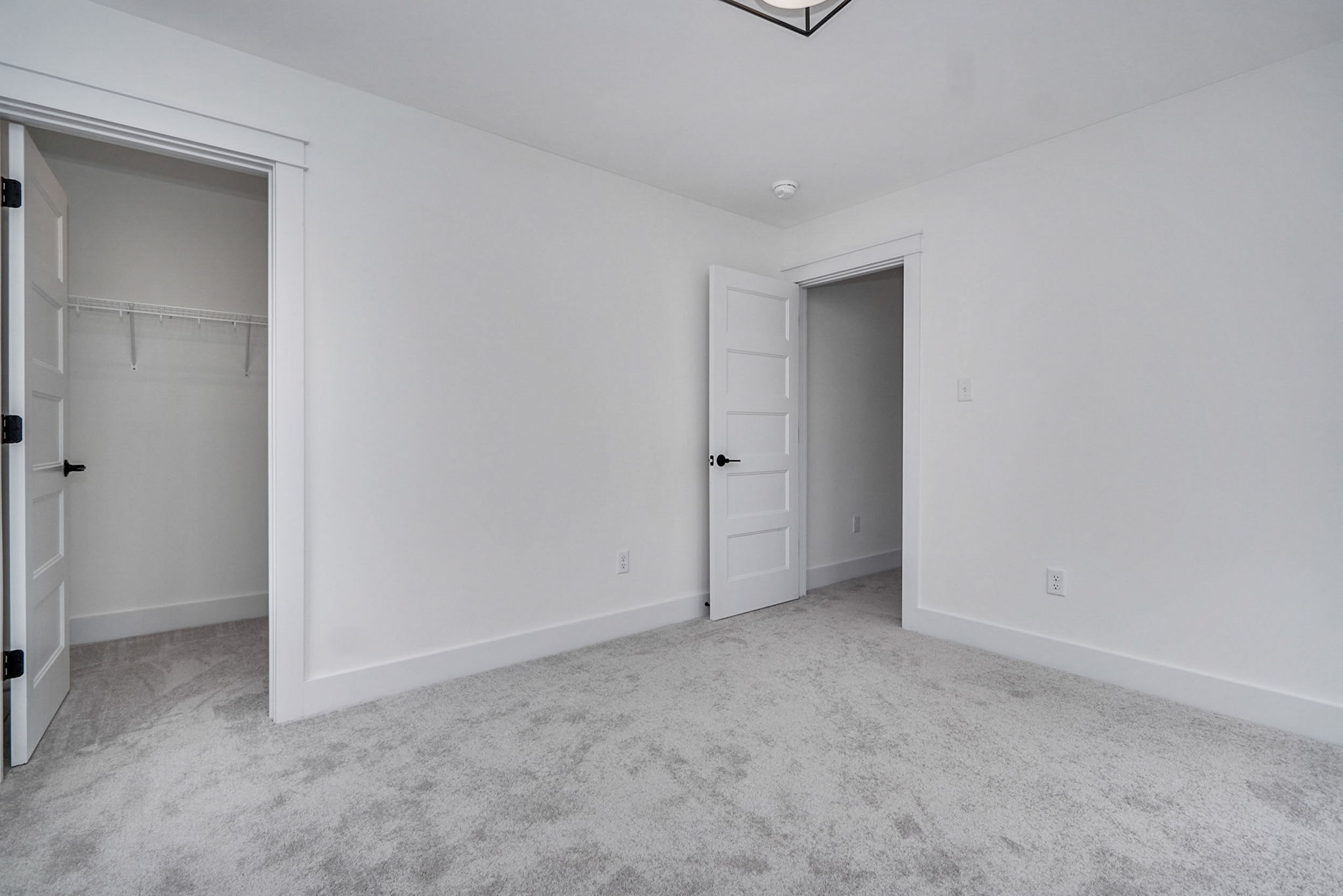 A clean, empty room with white walls, gray carpet, a closet with an open door on the left, and another open door on the right.