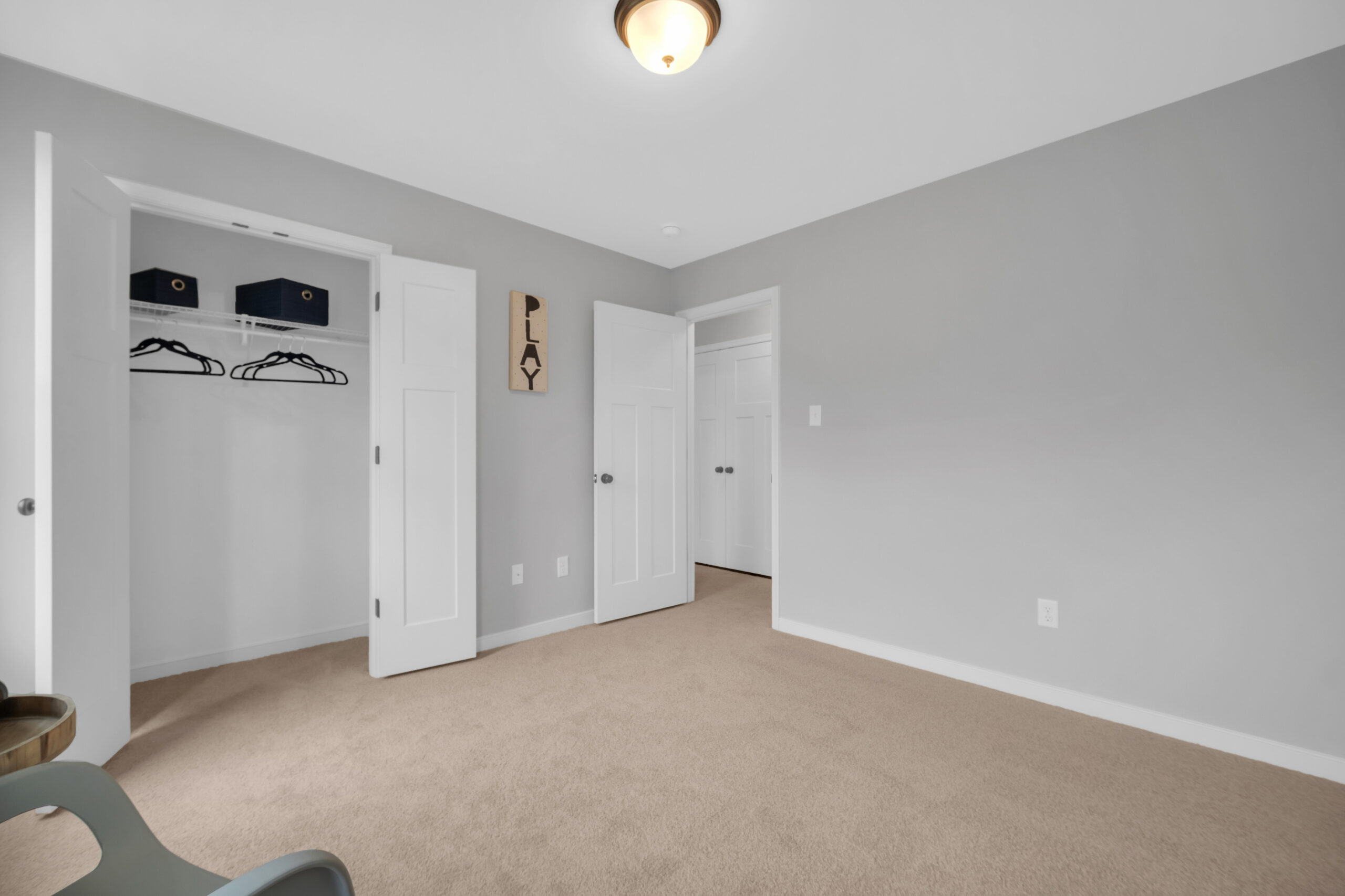 Empty room with beige carpet, white walls, and three closed doors. one wall features a small shelf with decorative items and a sign saying "play".