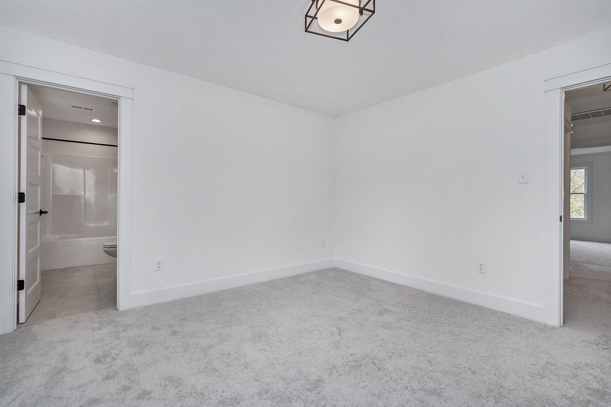 A white room with gray carpet, minimal furniture, and two doorways; one leading to a bathroom and the other to a hallway or another room.