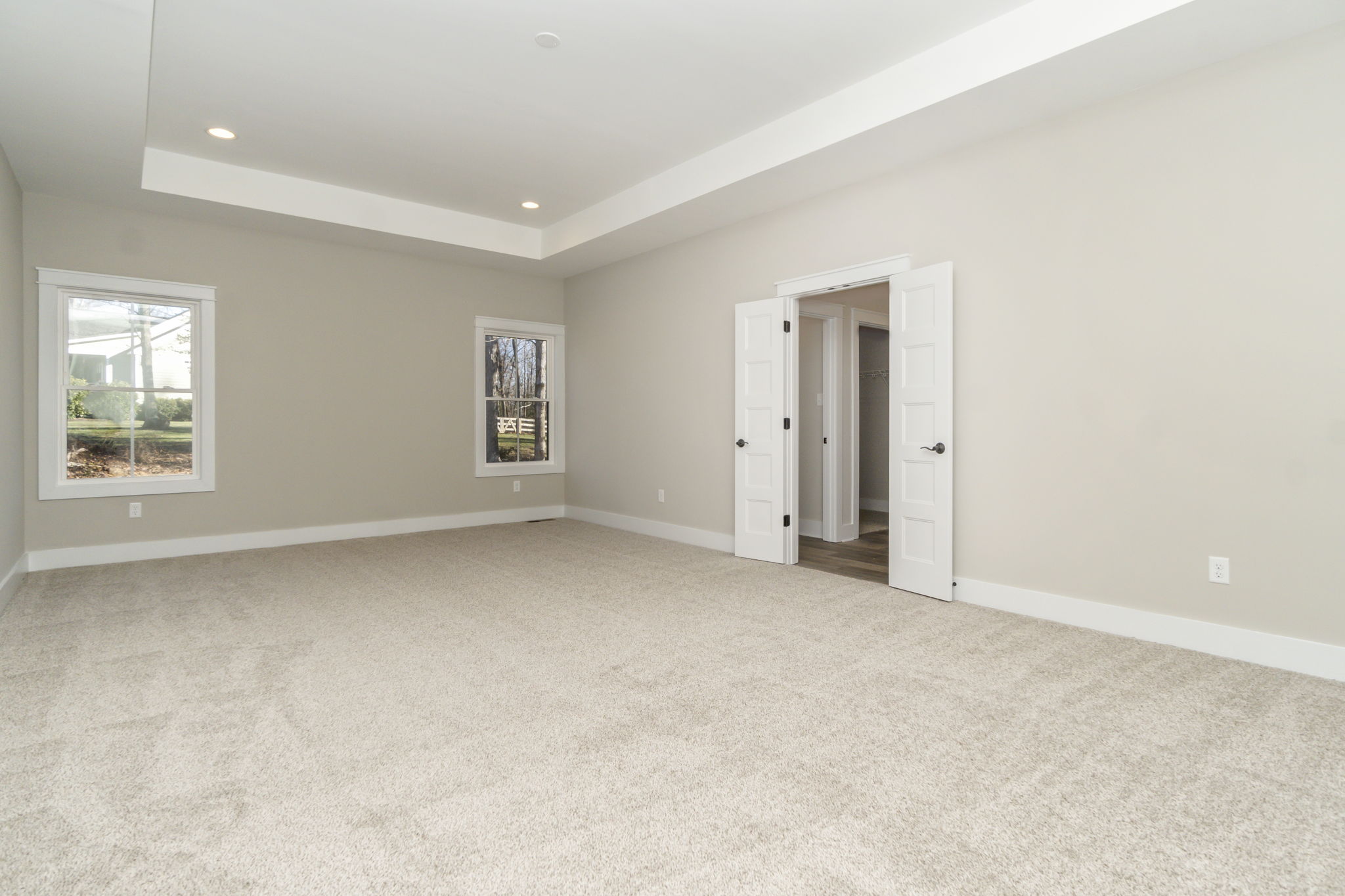 Empty living room with beige carpet, white walls, multiple windows, and open white doors.
