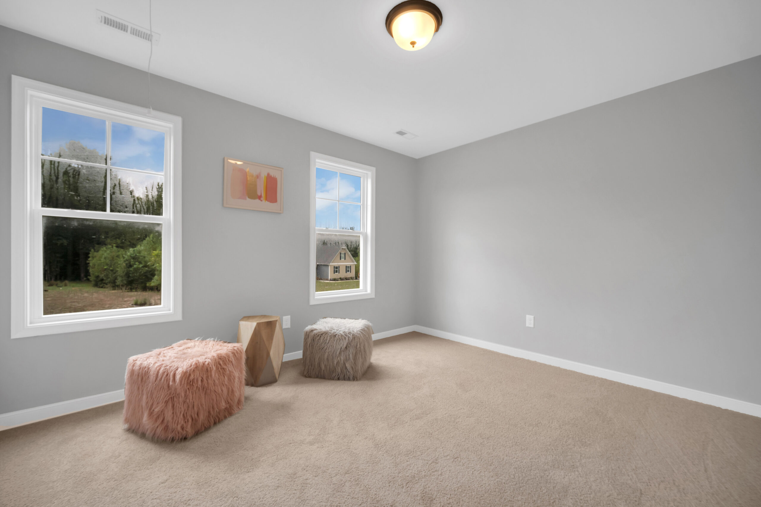 A minimalist room with two windows, a beige carpet, two textured ottomans, a geometric wooden stool, a framed wall picture, and a ceiling light fixture.