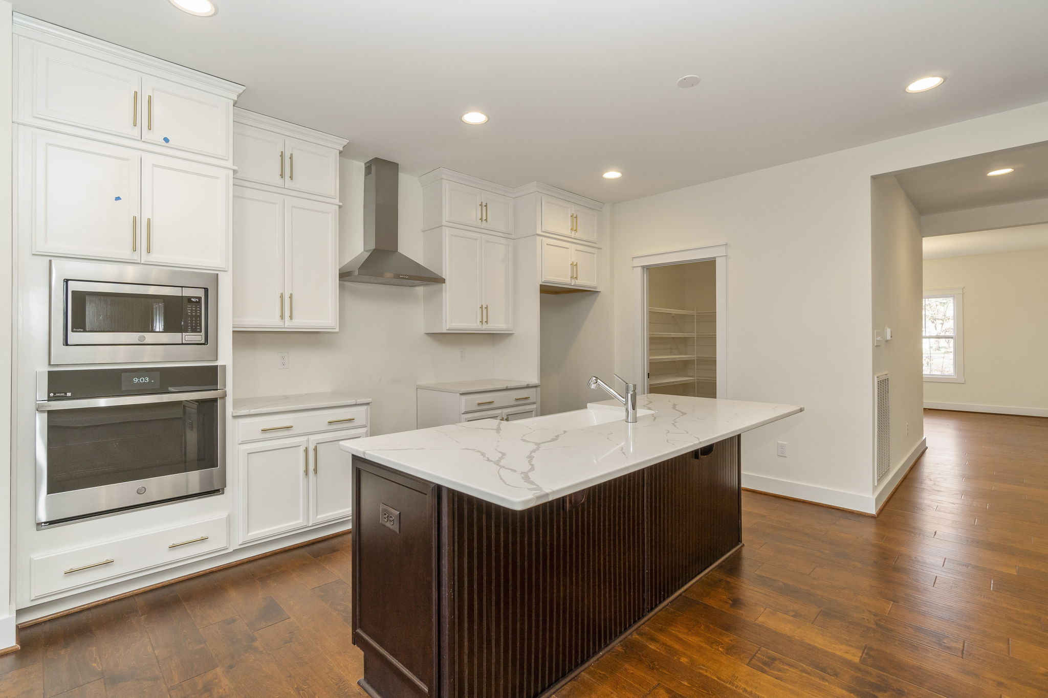 Modern kitchen with white cabinets, stainless steel appliances, a central island with a sink, and hardwood flooring.