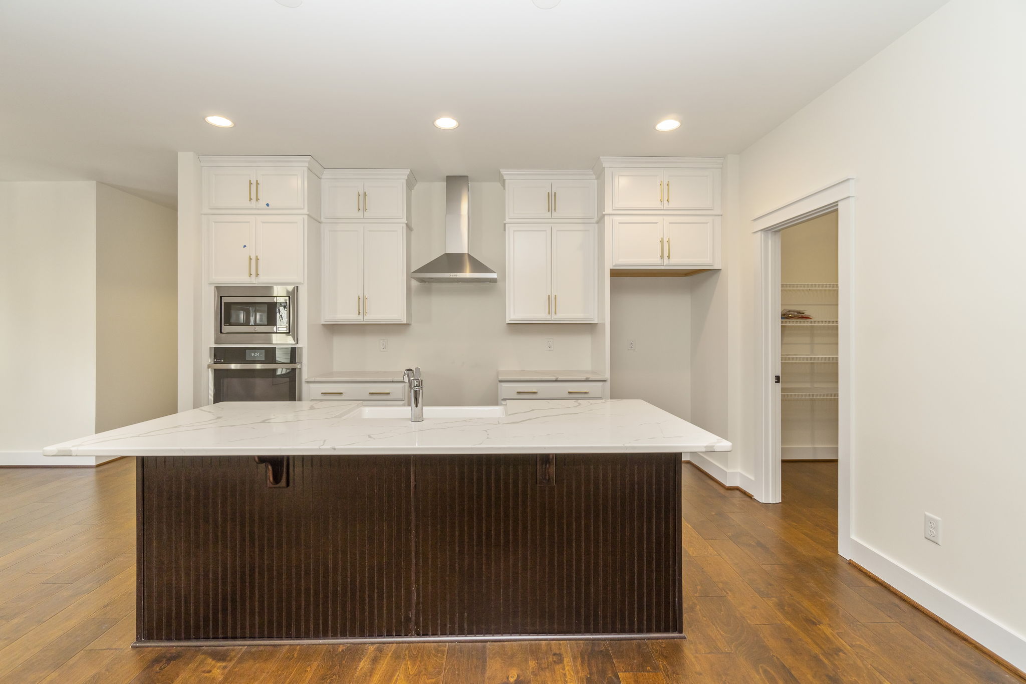 Modern kitchen with white cabinetry, a large island with a dark base, built-in appliances, and hardwood floors.