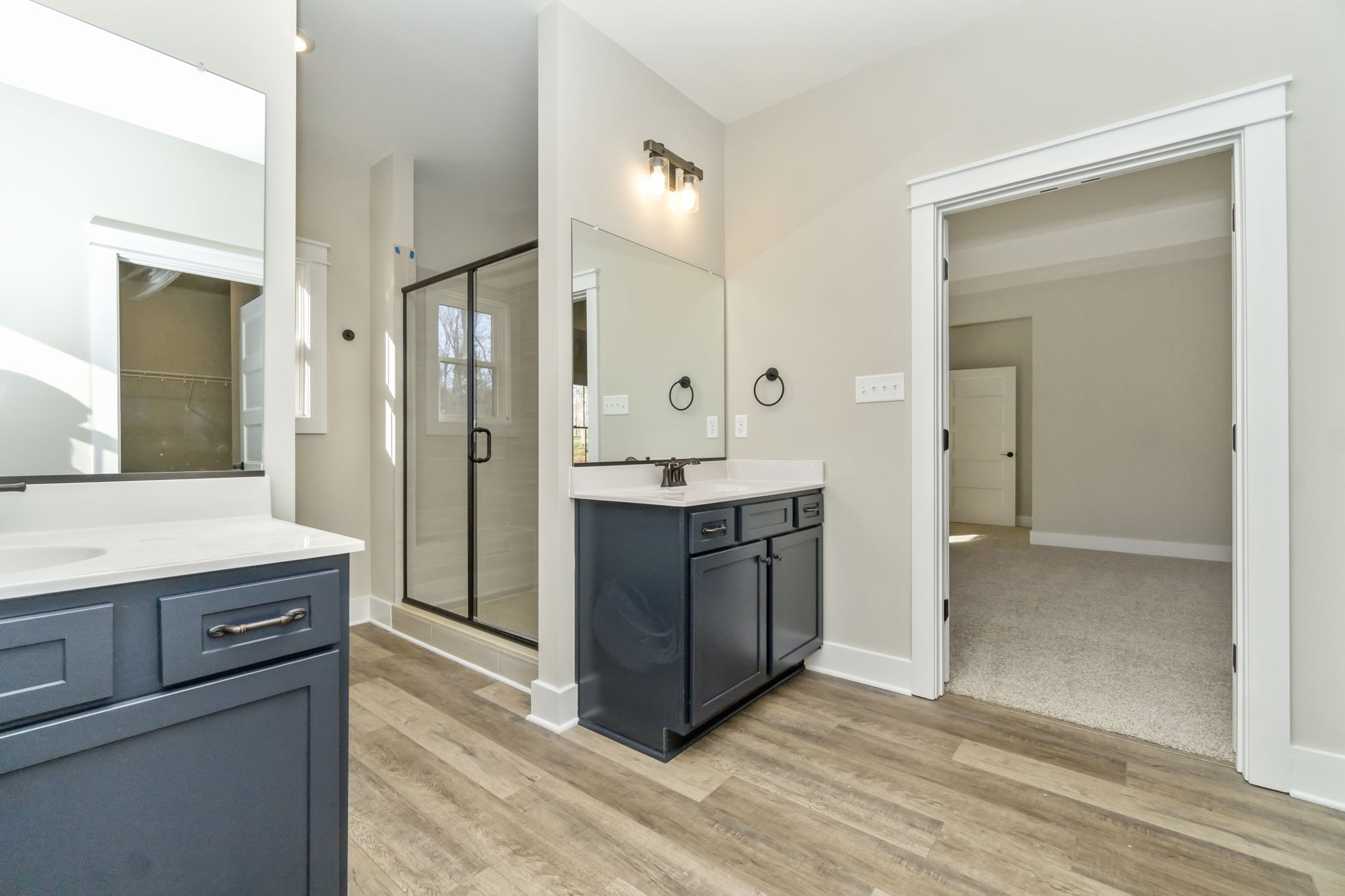 Modern bathroom with a dark blue vanity, white walls, and glass shower doors next to a carpeted bedroom entrance.