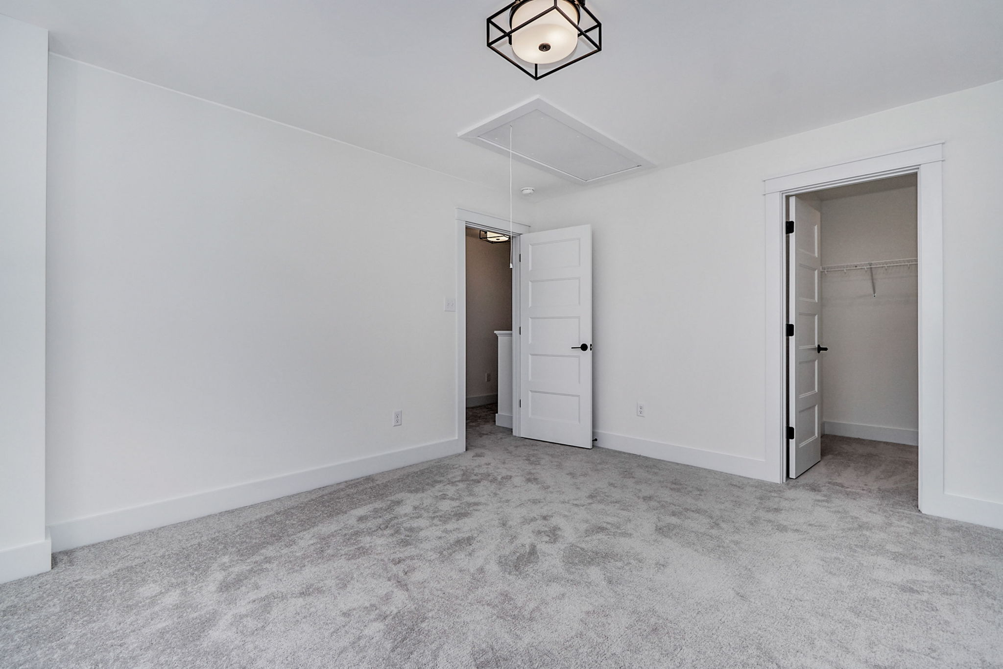 A white room with carpeted floor, a ceiling light, two open doors leading to a closet and another room.