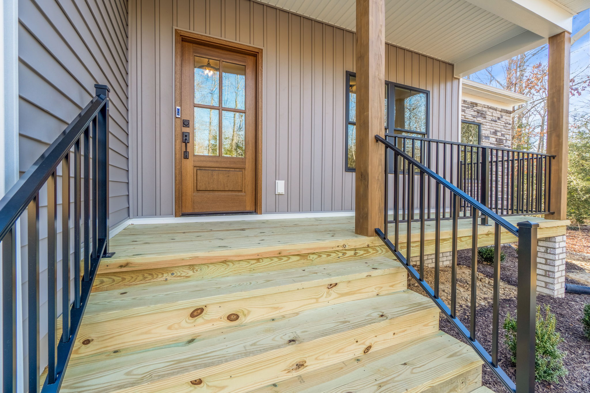 Front porch of a modern home with new wooden steps and a brown door, featuring black metal railings and a beige siding exterior.