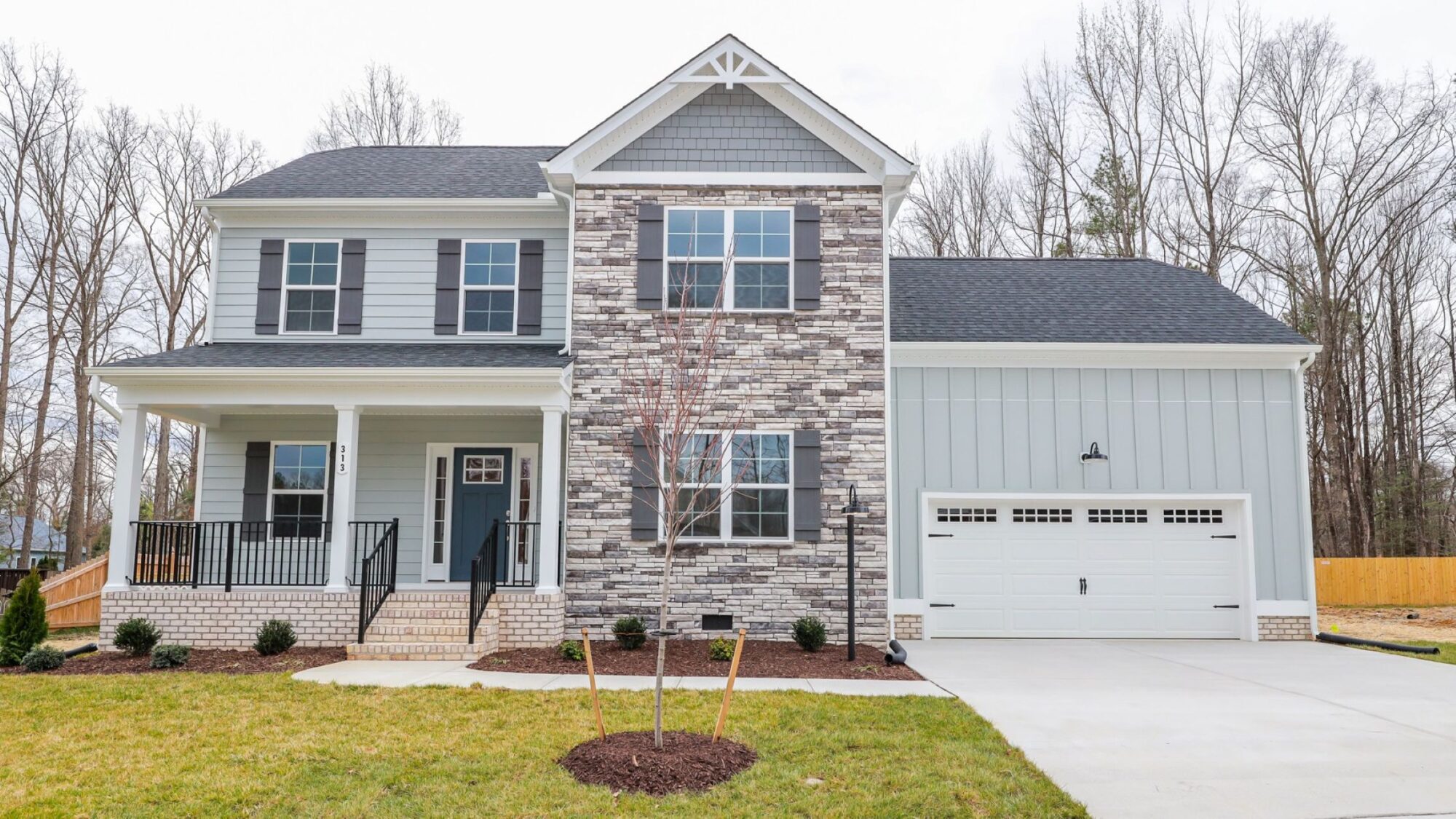 Two-story house with stone facade, porch, and attached garage surrounded by trees and lawn.