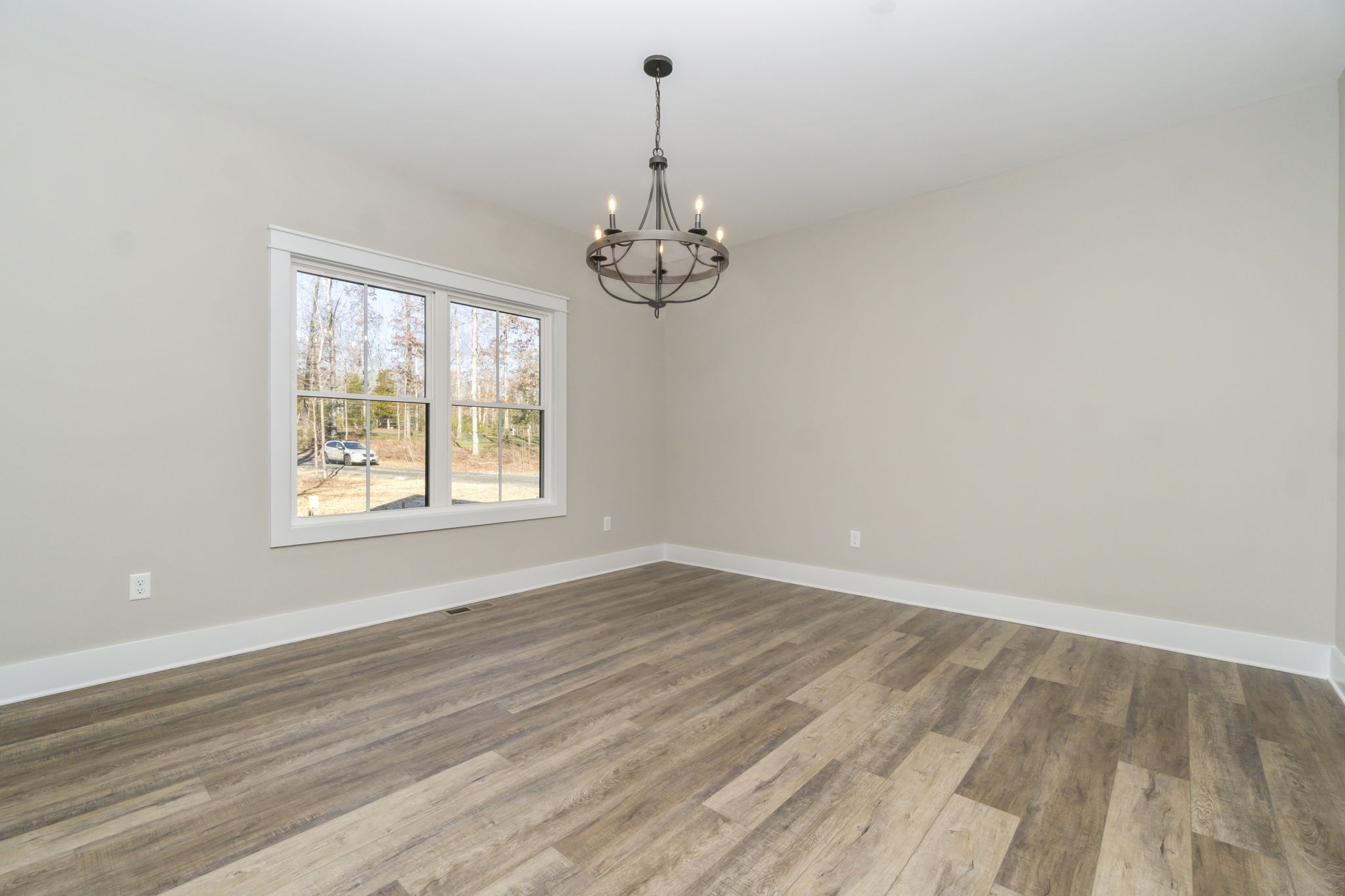 Empty modern room with grey wooden flooring, a large window, and a black chandelier.
