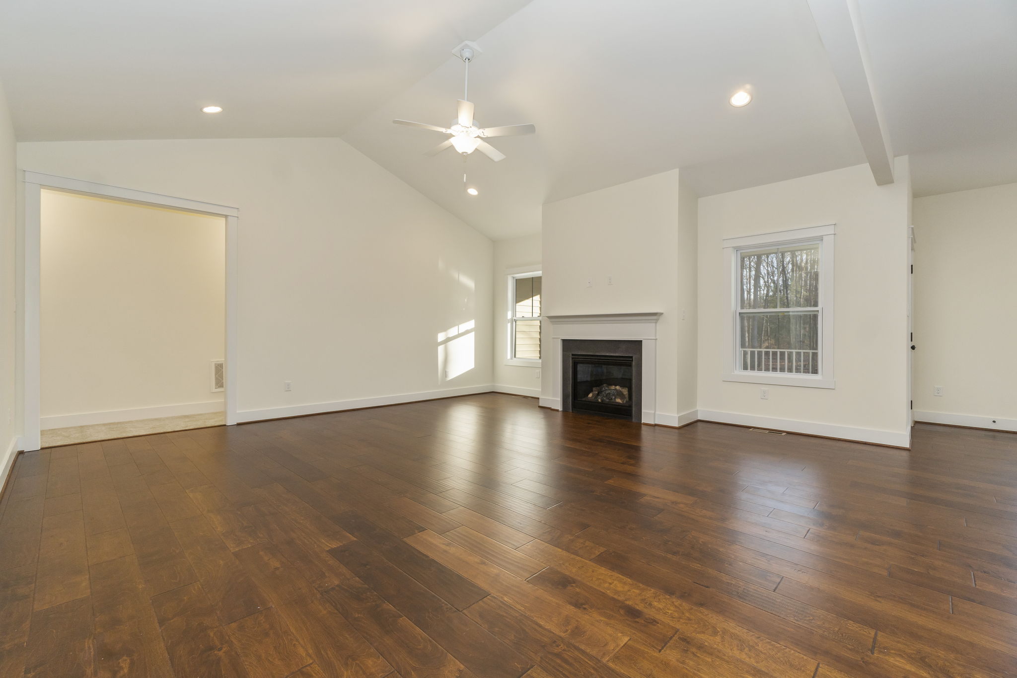 Spacious living room with hardwood floors, white walls, a fireplace, and multiple windows allowing natural light.