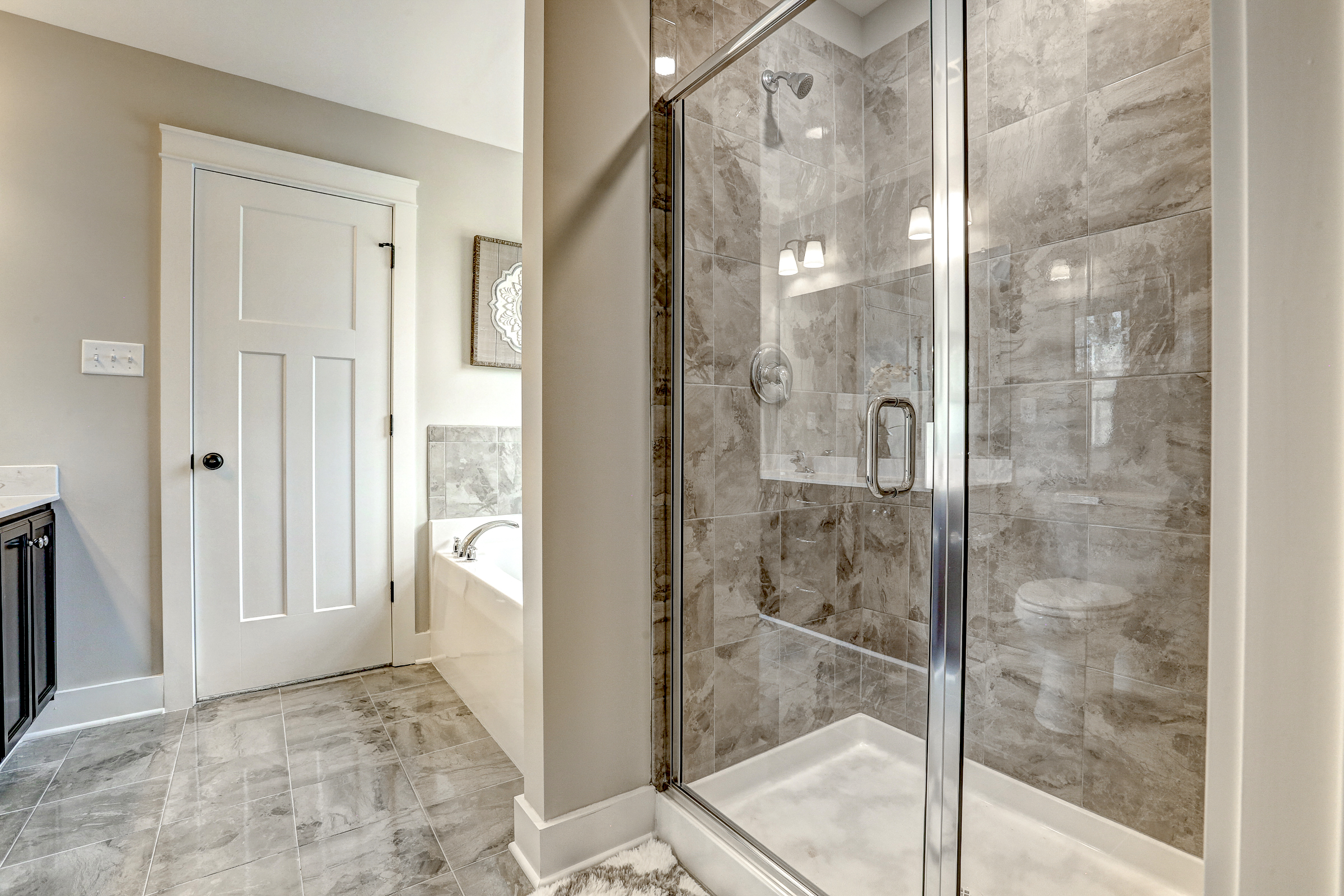 Modern bathroom with tiled flooring, a glass-enclosed shower, a bathtub, and a white door.