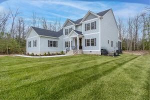 Two-story white house with black shutters, surrounded by a large, neatly mowed lawn and bordered by leafless trees under a clear blue sky.