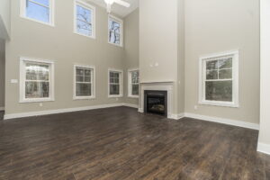 A spacious living room with high ceilings, multiple windows, a fireplace, and dark wooden flooring.