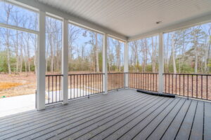 Covered porch with wooden flooring and black railings overlooking a forest with bare trees.
