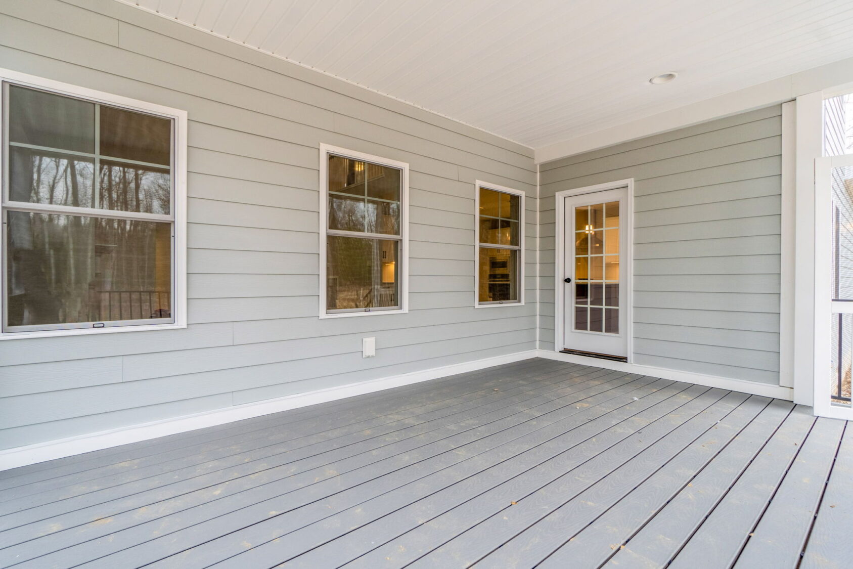 A gray-painted porch with three windows and a glass door leading inside. The ceiling and floor are made of light-colored wood.