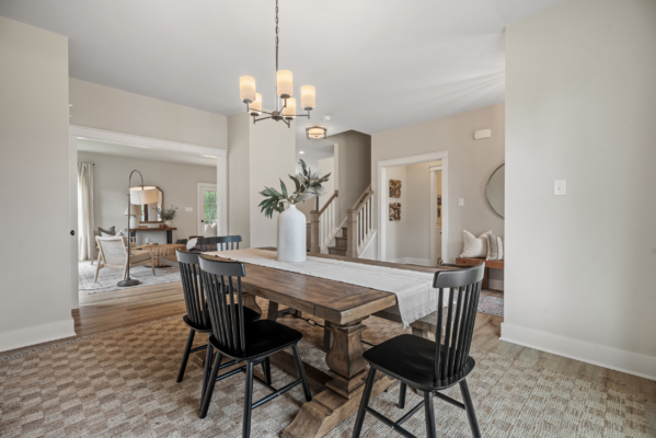 In the Haley Meadows collection, a modern dining room features a wooden table, black chairs, an elegant chandelier, and a stylish vase centerpiece.