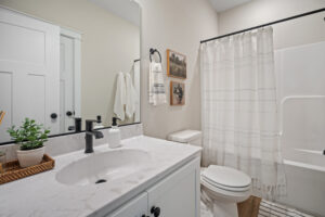 Modern bathroom in Haley Meadows with a white countertop, sink, toilet, and striped shower curtain. The decor seamlessly blends towels and plants for a refreshing touch.