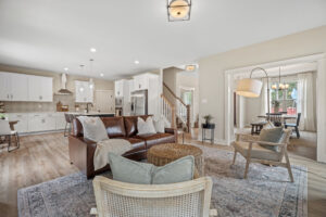 Discover the perfect living space at Haley Meadows, featuring a spacious open area with a brown leather sofa, a modern kitchen, and dining area. The light wood flooring ties the space together beautifully.